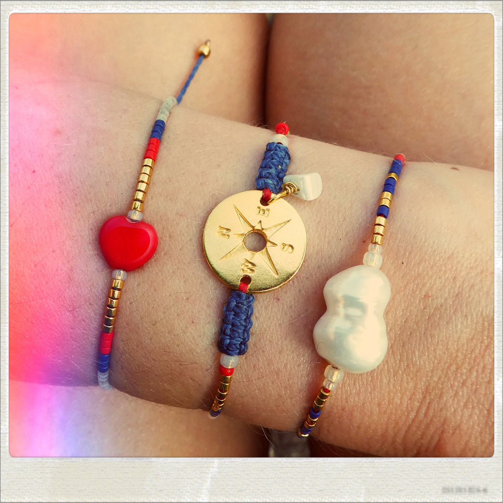 Peut inclure: Trois bracelets avec des perles rouges, blanches et bleues. Un bracelet présente un charme de boussole en or, un autre un charme de cœur rouge et le troisième un charme de perle blanche.