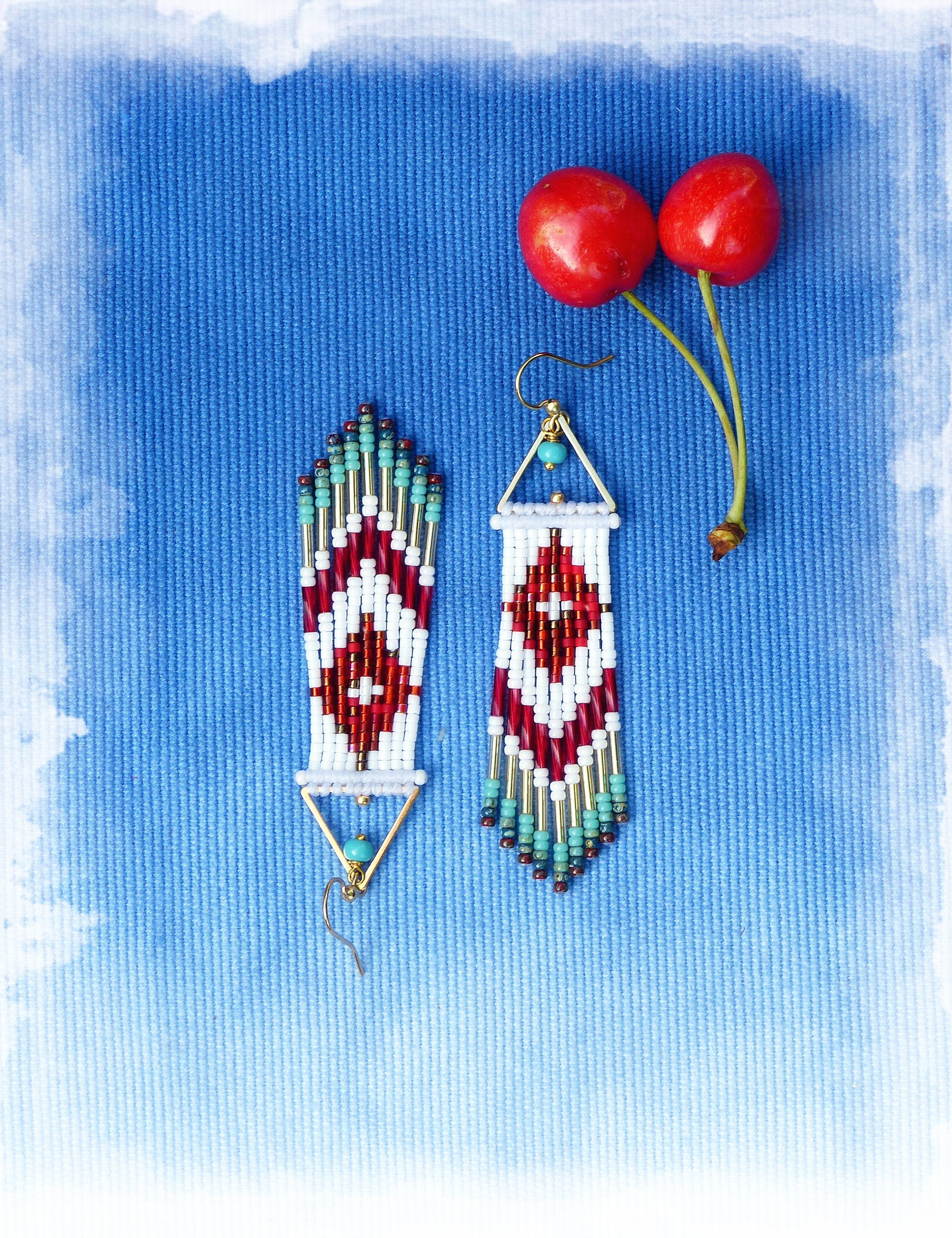 Peut inclure: Une paire de boucles d'oreilles en perles avec un motif géométrique en rouge, blanc et turquoise. Les boucles d'oreilles sont suspendues à des crochets dorés et ont une frange de perles en bas.
