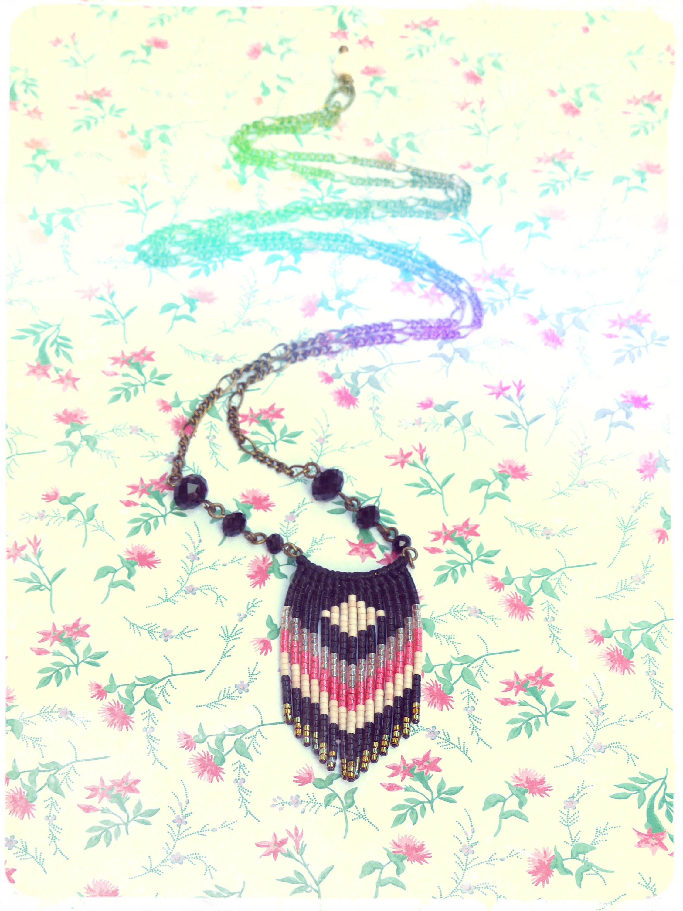 Peut inclure: Un collier de perles avec un motif géométrique noir, blanc et rose. Le collier est fait de petites perles et a une frange au bas.
