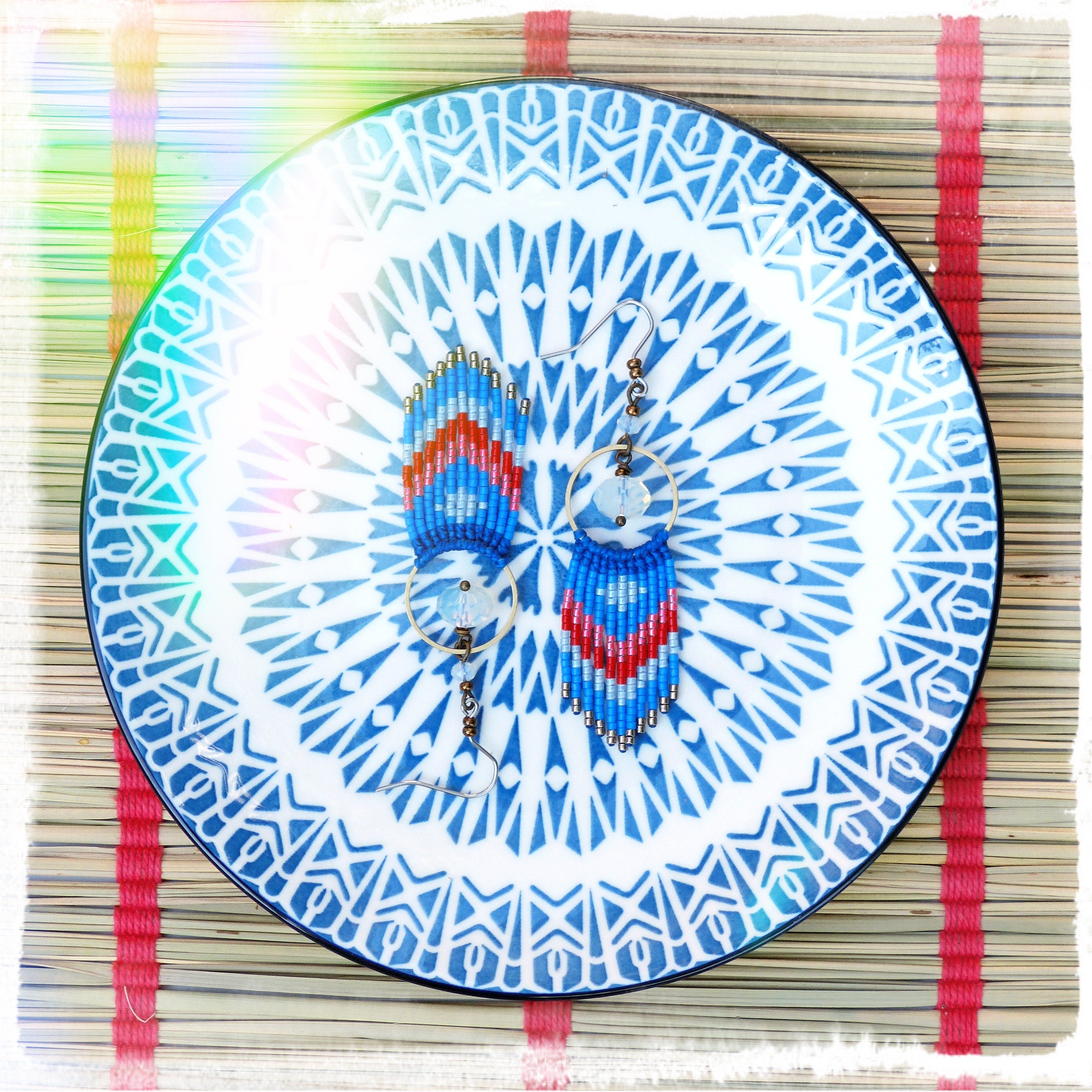 Peut inclure: Une paire de boucles d'oreilles en perles bleues et rouges avec une assiette à motifs blancs et bleus en arrière-plan.