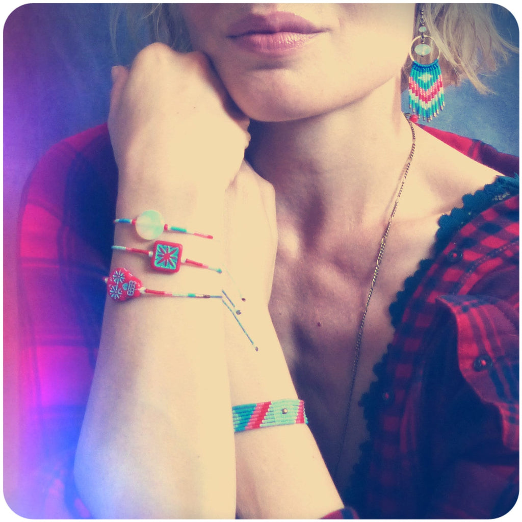 Peut inclure: Plusieurs bracelets colorés avec des motifs géométriques et des détails perlés. Les bracelets sont rouges, turquoise et blancs. L'image montre également une paire de boucles d'oreilles assorties avec un design à franges.
