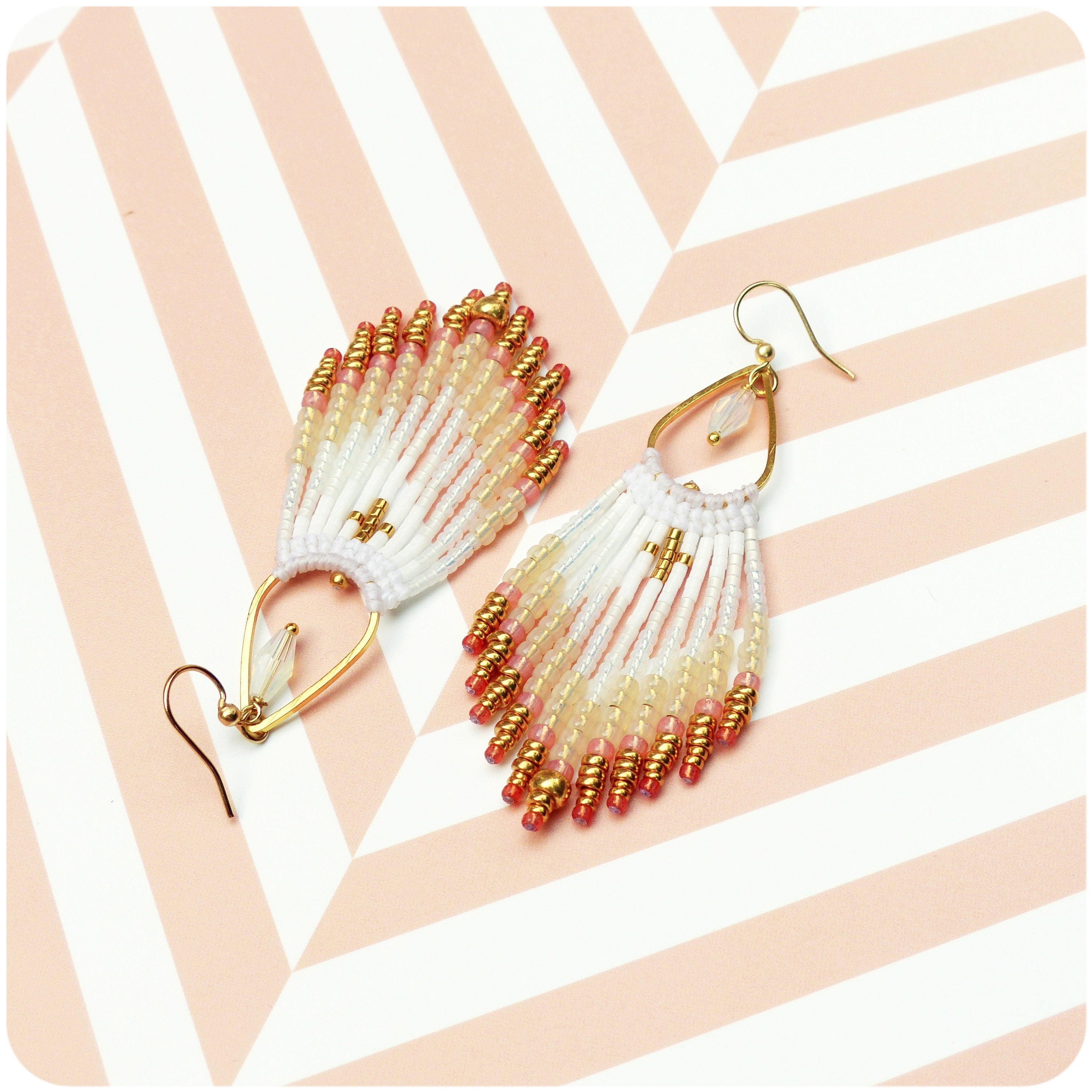 Peut inclure: Une paire de boucles d'oreilles pendantes dorées avec des franges de perles blanches et roses. Les boucles d'oreilles ont une forme de larme et sont faites de petites perles délicates.