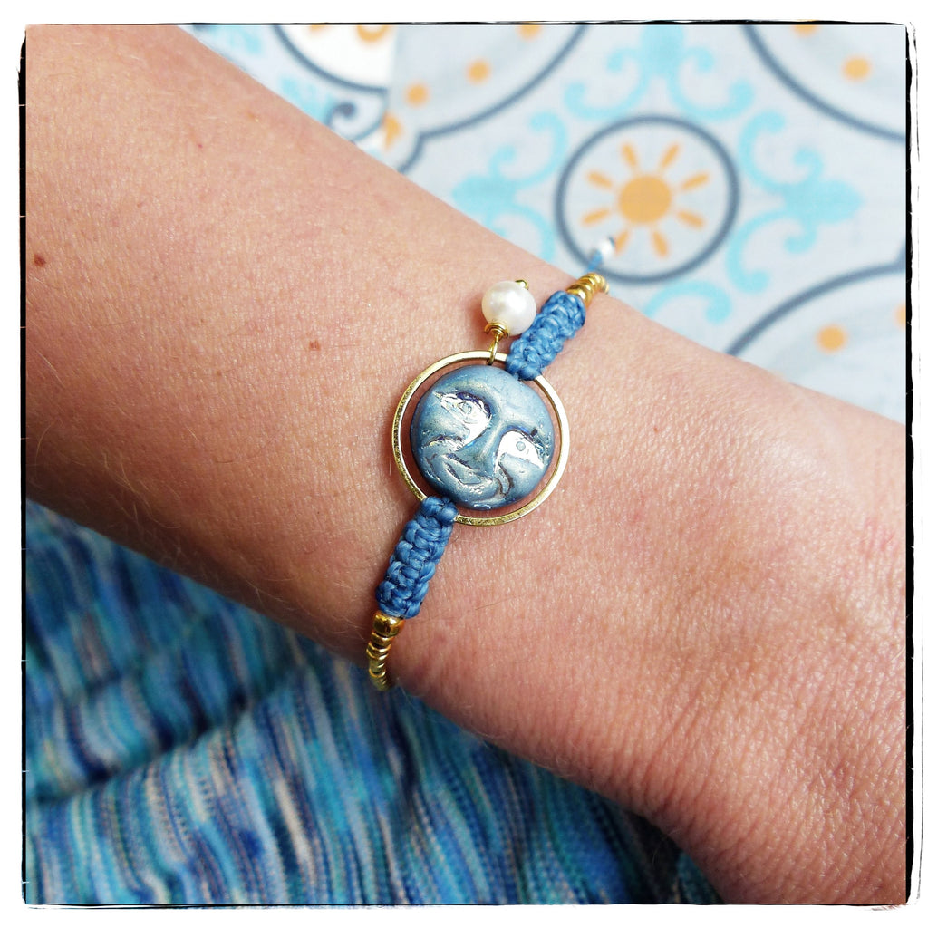 Peut inclure: Un bracelet bleu et or avec un charme visage de lune et un accent de perle blanche. Le bracelet est fait de cordon tressé et a un fermoir en or.