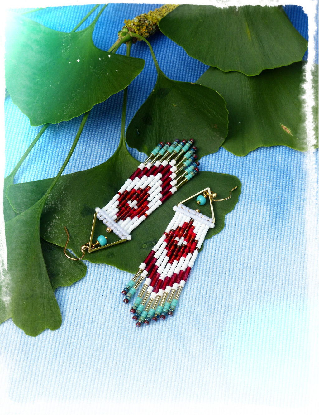 Peut inclure: Une paire de longues boucles d'oreilles en perles avec un motif géométrique. Les boucles d'oreilles sont faites de perles blanches, rouges et turquoise et ont des accents dorés. Les boucles d'oreilles sont suspendues sur un fond bleu.