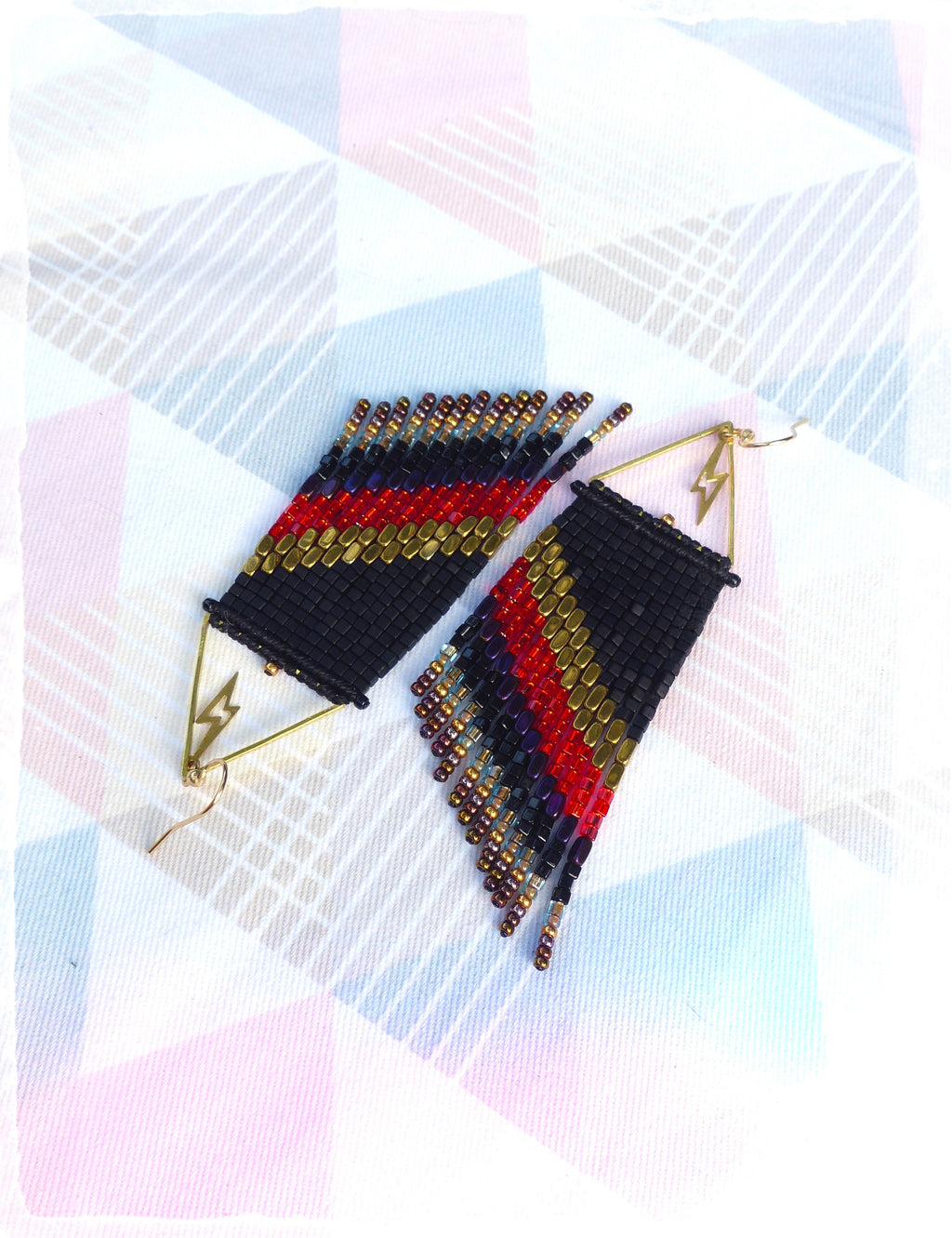 Peut inclure: Une paire de boucles d'oreilles perlées faites à la main. Les boucles d'oreilles sont noires avec des rayures rouges, dorées et violettes. Chaque boucle d'oreille a un charme en forme d'éclair doré et un crochet d'oreille doré.
