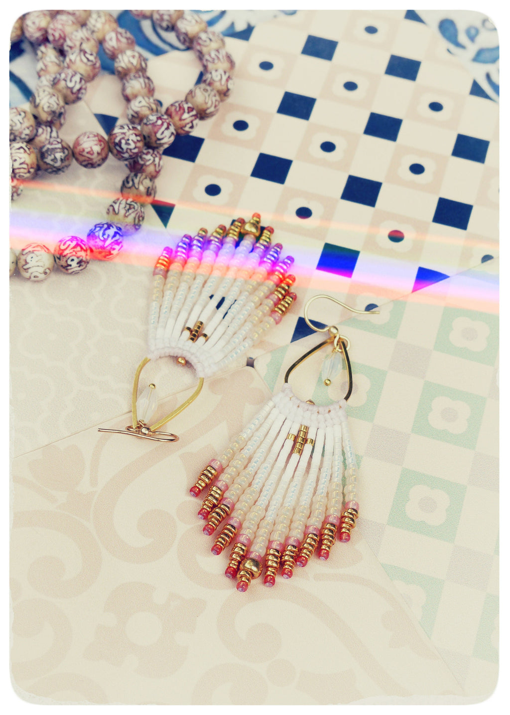 Peut inclure: Une paire de boucles d'oreilles en perles blanches et dorées avec des accents roses et dorés. Les boucles d'oreilles sont pendantes et ont un design en forme de glands.