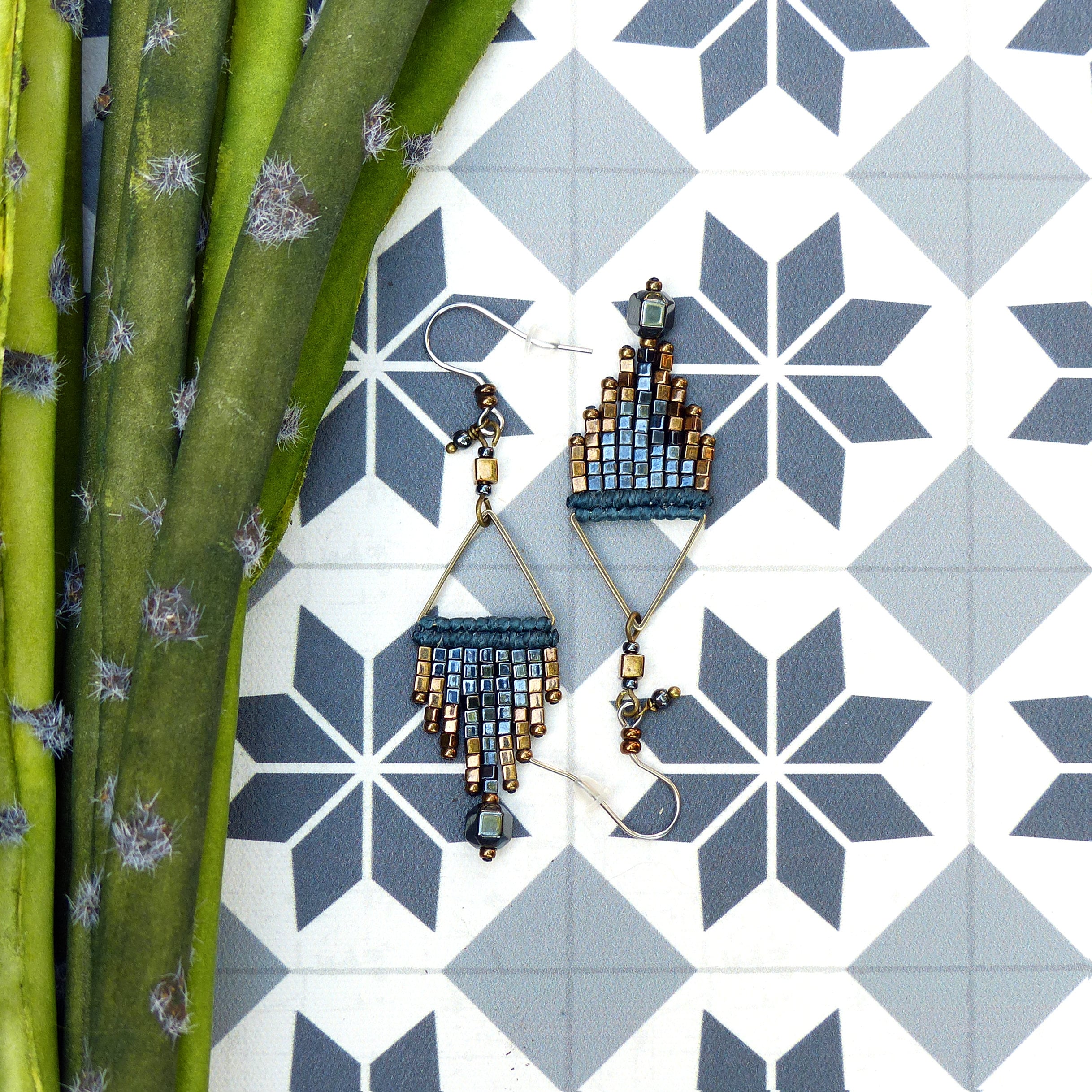 Peut inclure: Une paire de boucles d'oreilles pendantes avec un design géométrique. Les boucles d'oreilles sont faites de perles bleues et dorées et ont une forme triangulaire. 