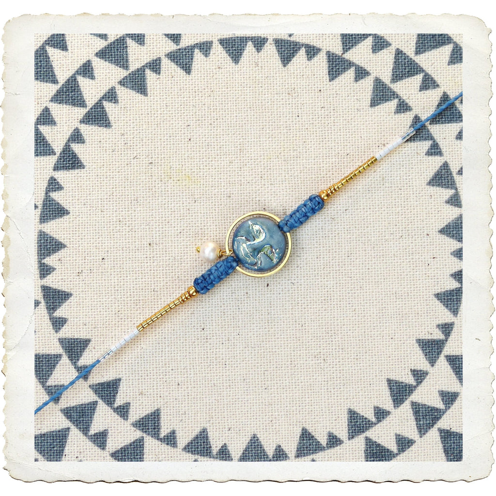 Peut inclure: Un bracelet bleu et or avec un charme rond bleu et blanc représentant un motif stylisé. Le bracelet est sur un fond blanc avec un motif bleu et blanc.