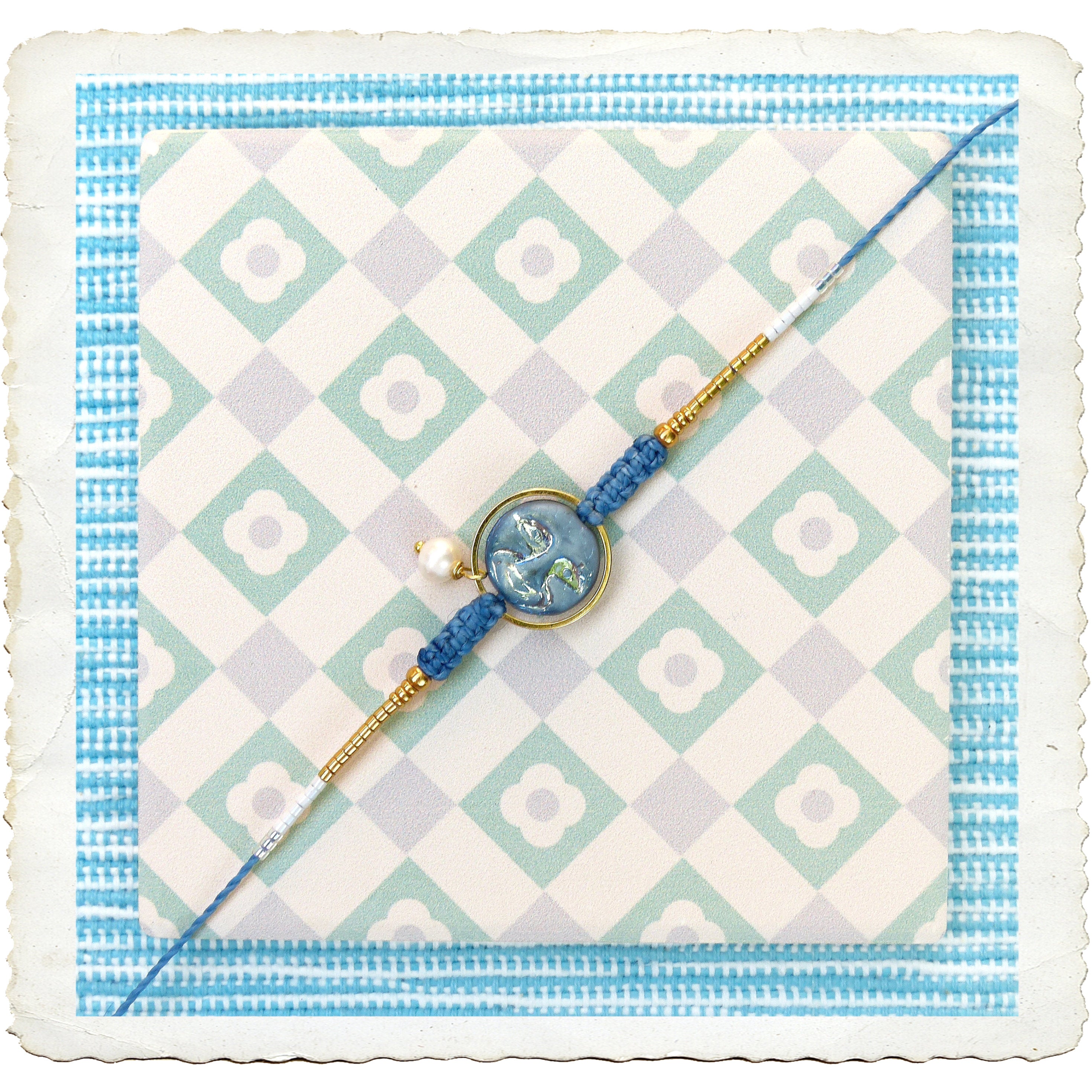 Peut inclure: Un bracelet bleu et or avec un charme de perle blanche et un charme à motif bleu et or. Le bracelet est sur un fond blanc avec un motif à carreaux bleus et verts.