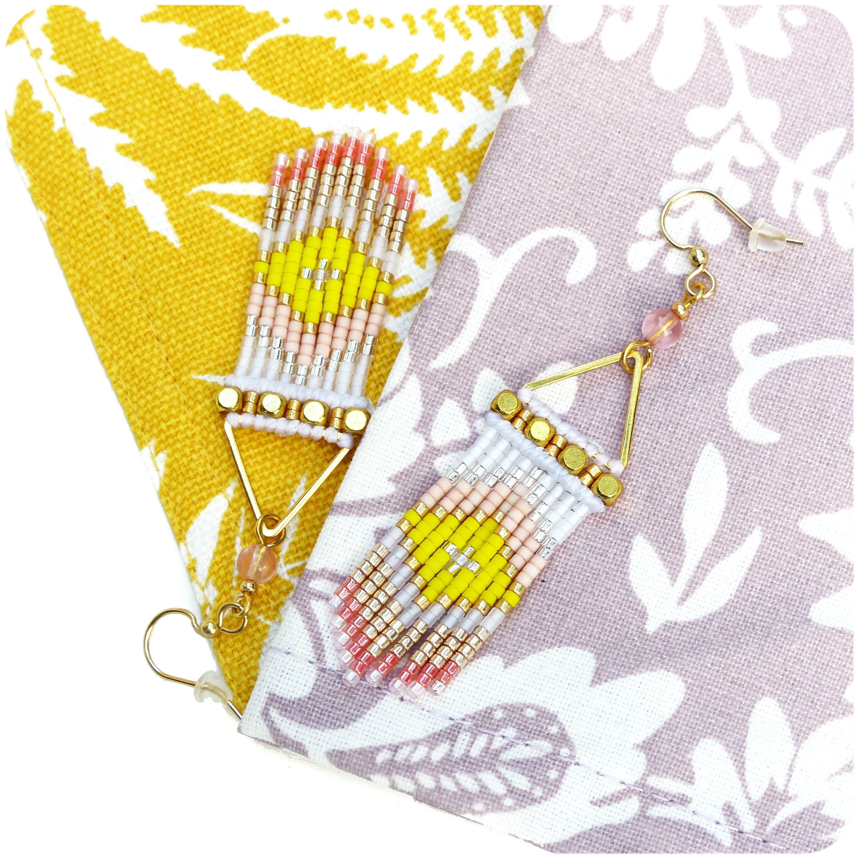 Peut inclure: Une paire de boucles d'oreilles triangulaires dorées avec des franges de perles roses, blanches et jaunes. Les boucles d'oreilles sont sur un fond de tissu à motifs.