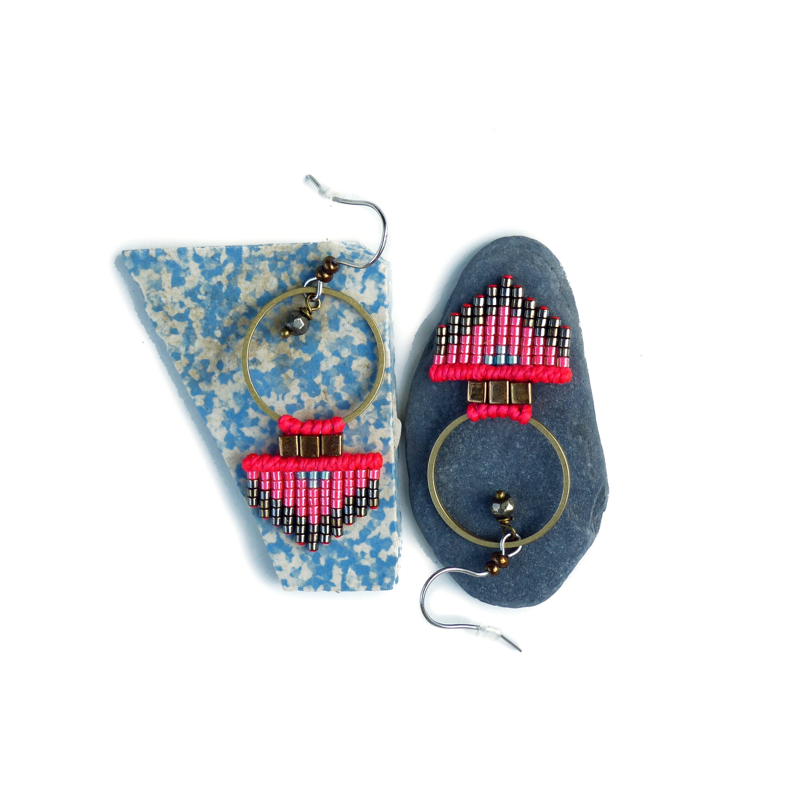 Peut inclure: Une paire de boucles d'oreilles en perles roses et argentées avec un motif géométrique. Les boucles d'oreilles sont suspendues à une pierre grise.