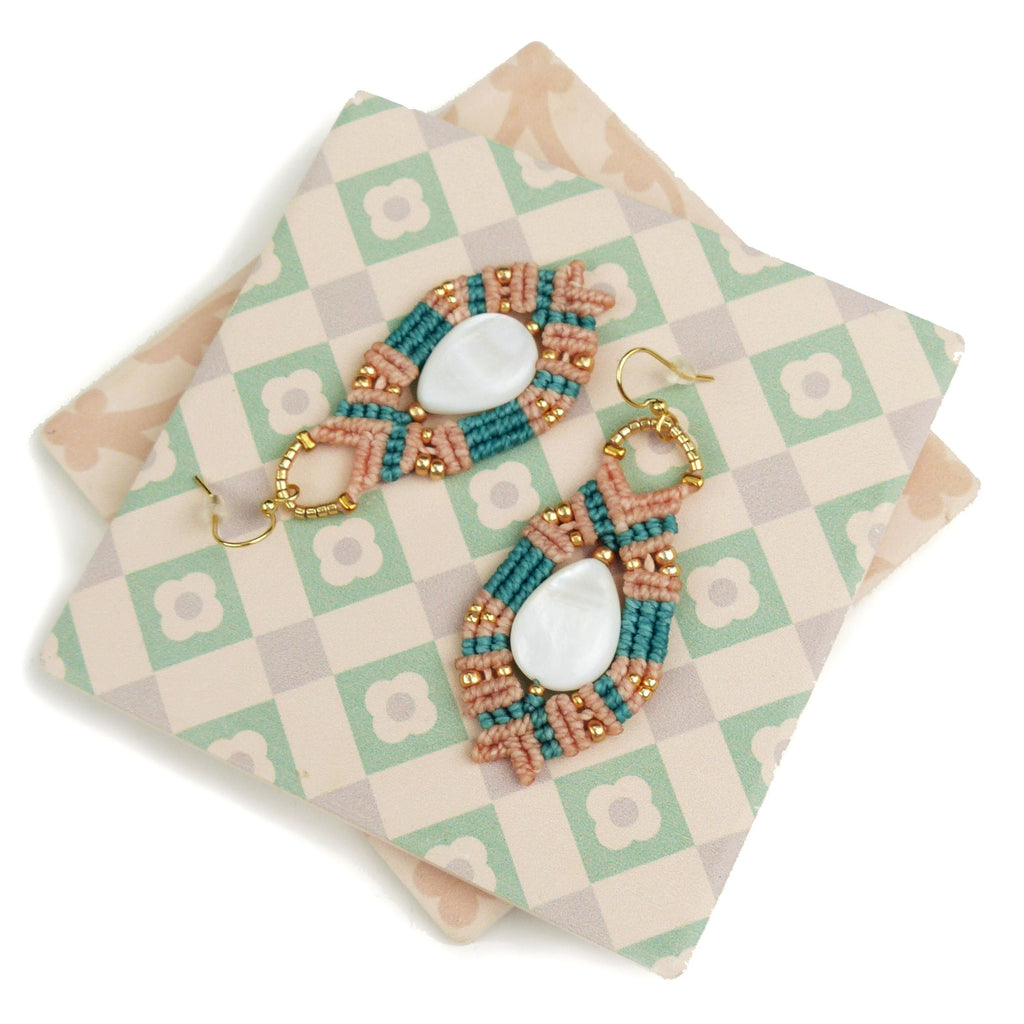 Peut inclure: Une paire de boucles d'oreilles faites à la main avec un design en macramé pêche et turquoise et des accents de coquillages blancs.