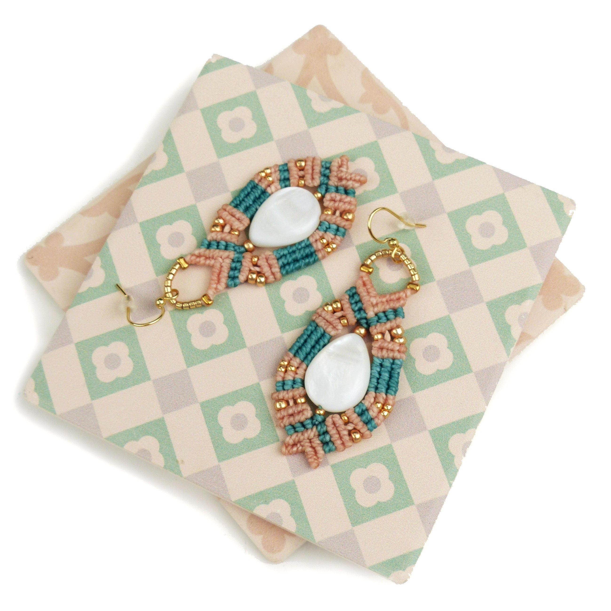 Peut inclure: Une paire de boucles d'oreilles faites à la main avec un design en macramé pêche et turquoise et des accents de coquillages blancs.