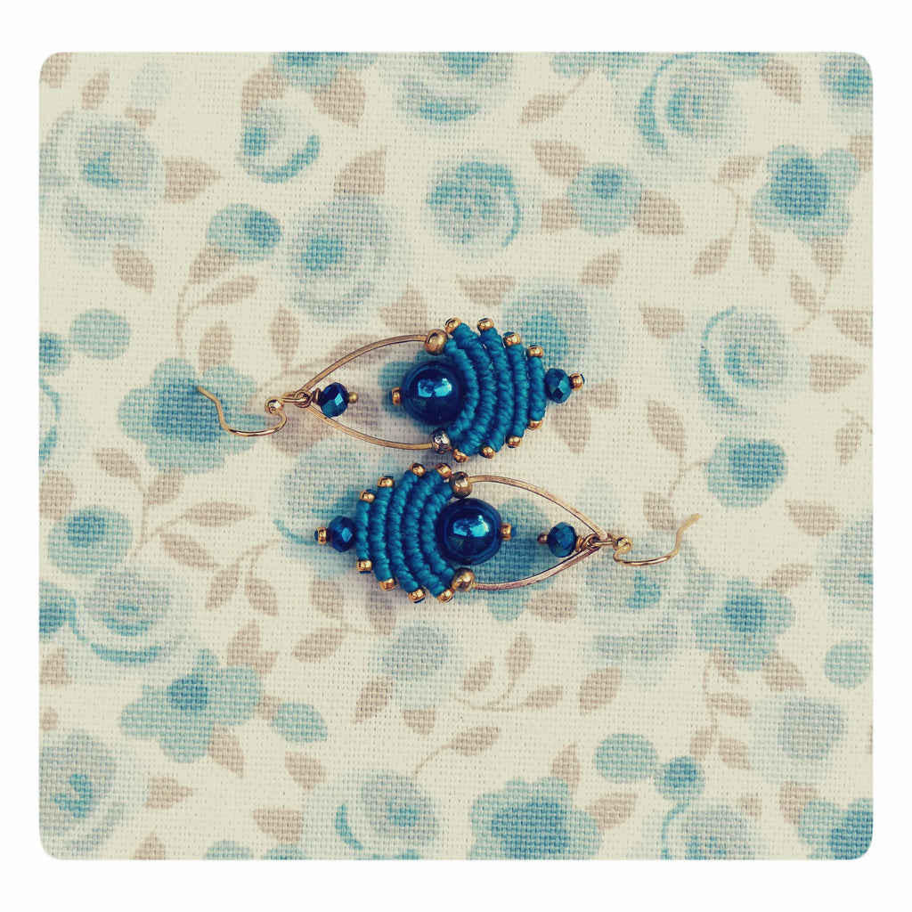 Peut inclure: Une paire de boucles d'oreilles bleues et dorées avec un motif perlé. Les boucles d'oreilles sont faites de fil bleu et de fil doré, et présentent une perle bleu foncé au centre de chaque boucle d'oreille.