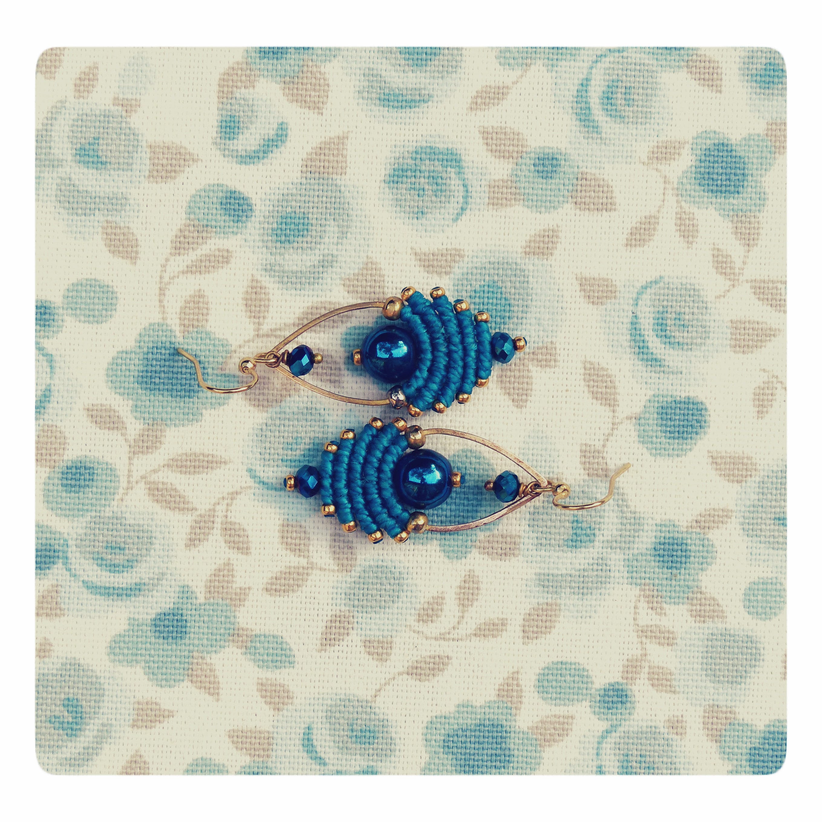 Peut inclure: Une paire de boucles d'oreilles bleues et dorées avec un motif perlé. Les boucles d'oreilles sont faites de fil bleu et de fil doré, et présentent une perle bleu foncé au centre de chaque boucle d'oreille.
