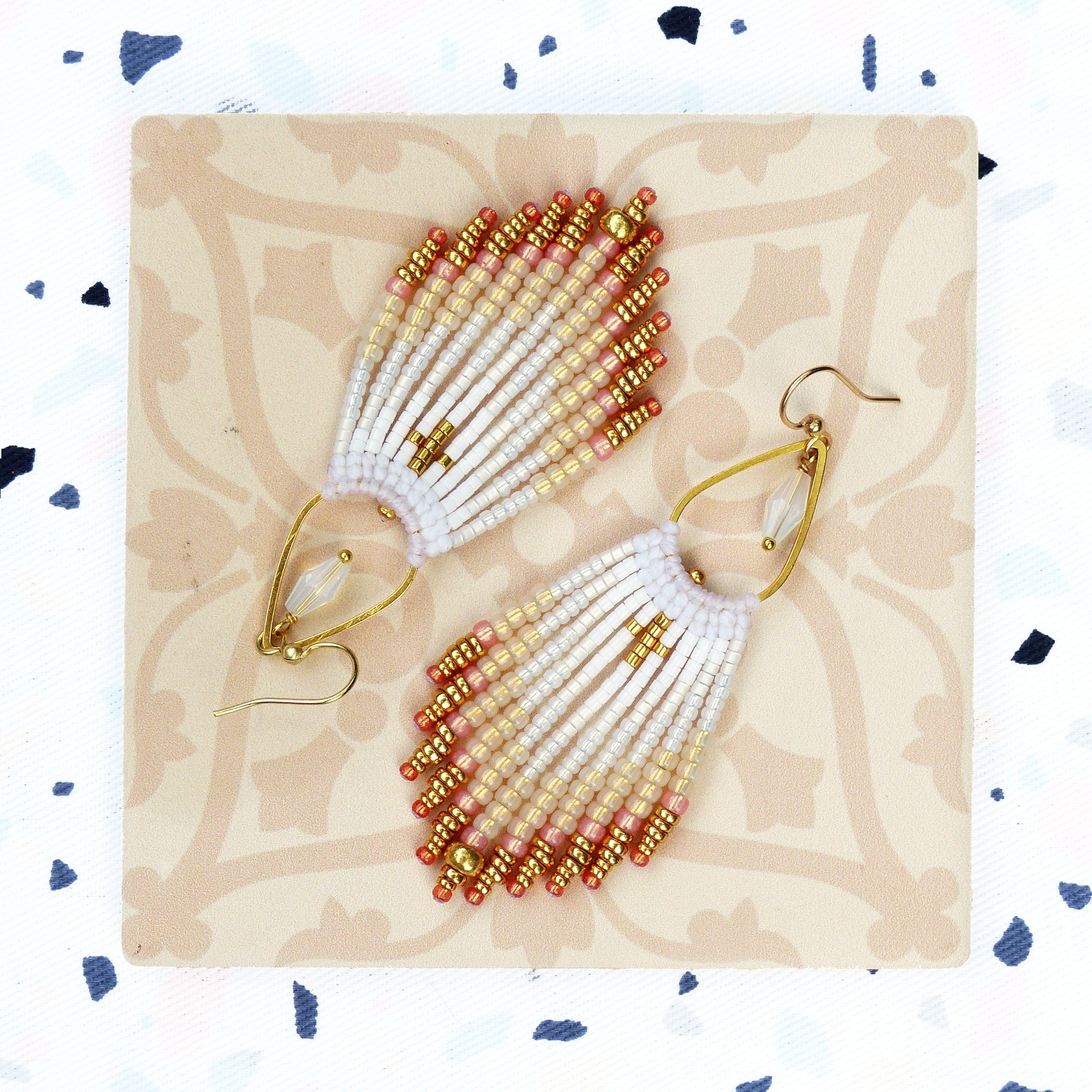 Peut inclure: Une paire de boucles d'oreilles pendantes avec une frange de perles blanches, pêche et dorées. Les boucles d'oreilles ont un crochet en or en forme de larme.