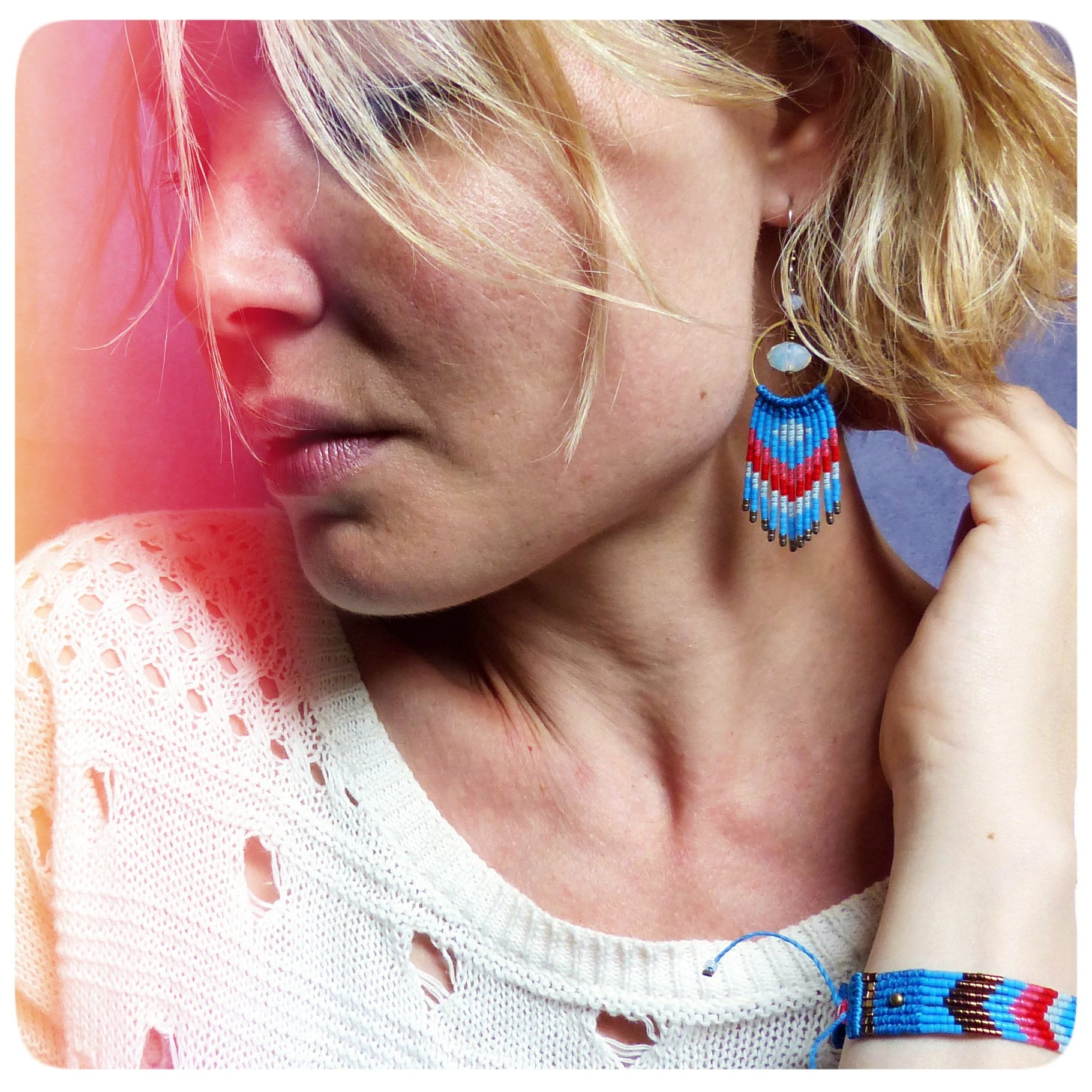 Peut inclure: Une femme portant un pull blanc avec une boucle d'oreille en frange de perles bleues et rouges et un bracelet en perles bleues et brunes.