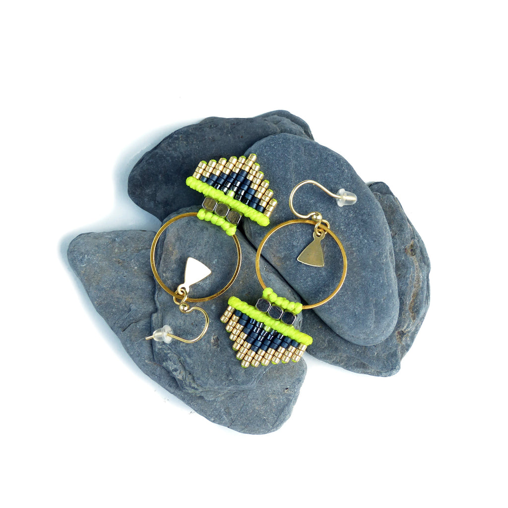 Peut inclure: Une paire de boucles d'oreilles créoles dorées avec des franges de perles noires et vert lime. Les boucles d'oreilles sont présentées sur deux pierres grises.