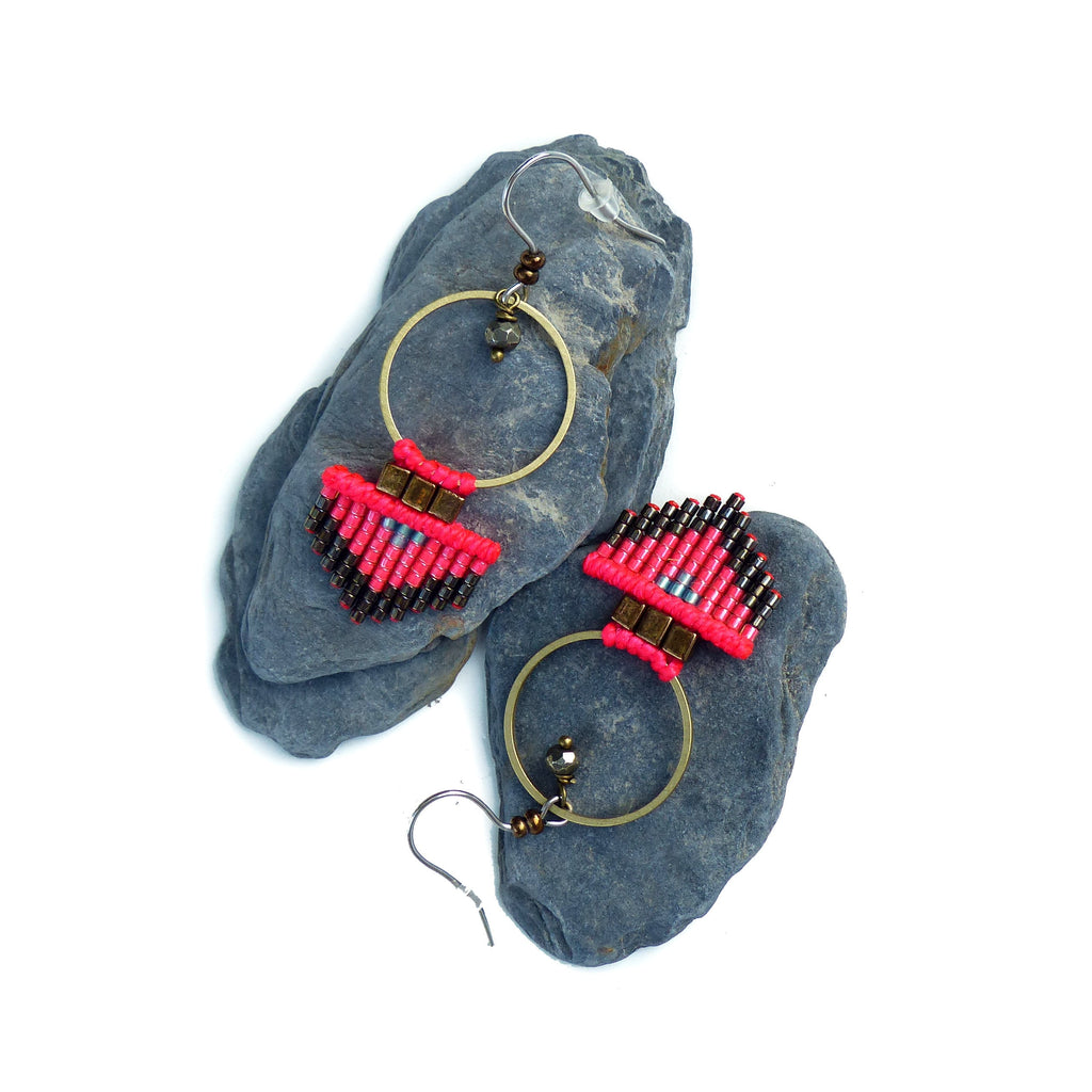 Peut inclure: Une paire de boucles d'oreilles en perles roses et brunes avec des anneaux dorés. Les boucles d'oreilles sont suspendues à des roches grises.