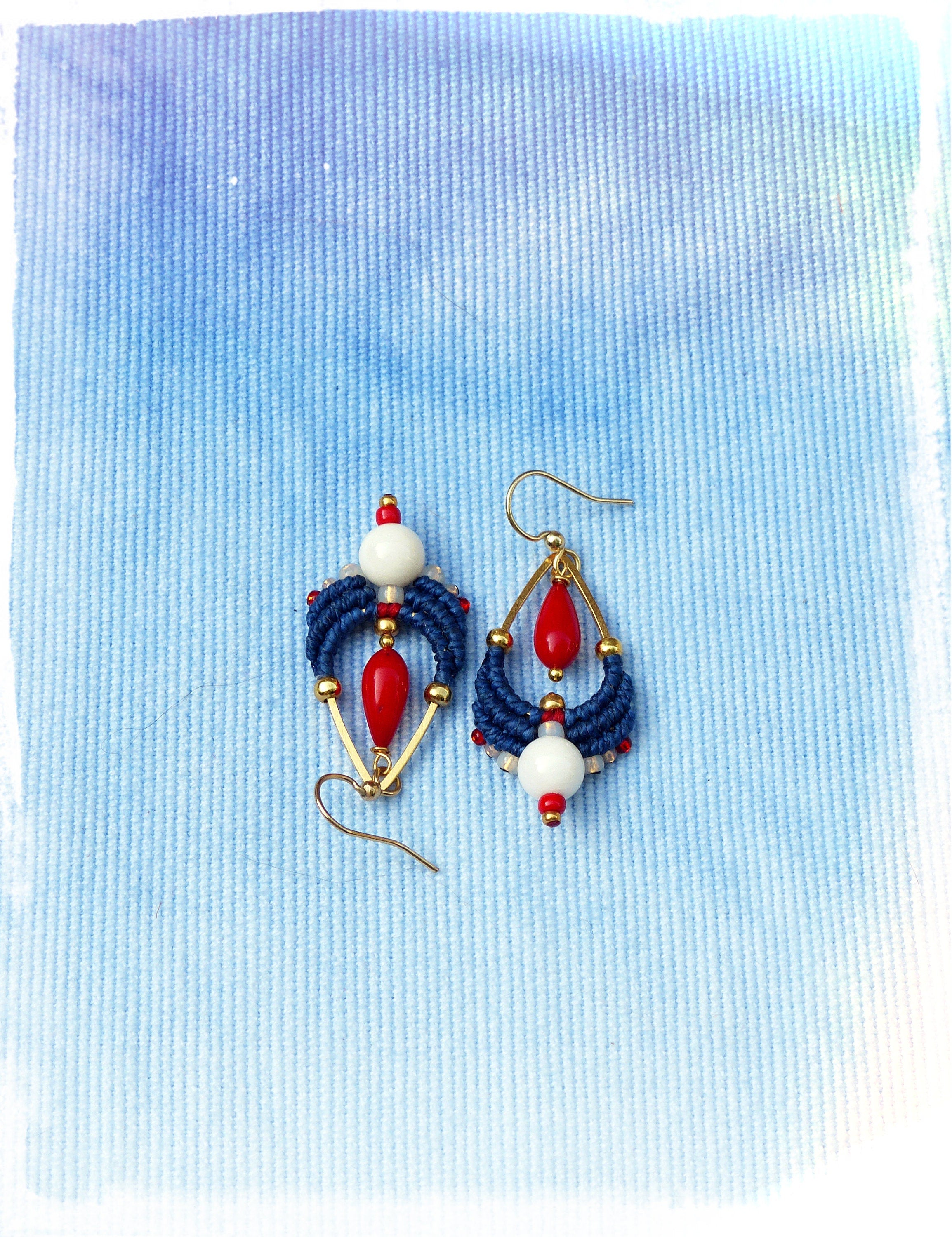 Peut inclure: Une paire de boucles d'oreilles pendantes avec des perles bleues, rouges et blanches. Les boucles d'oreilles ont une finition dorée et sont suspendues à un crochet doré.