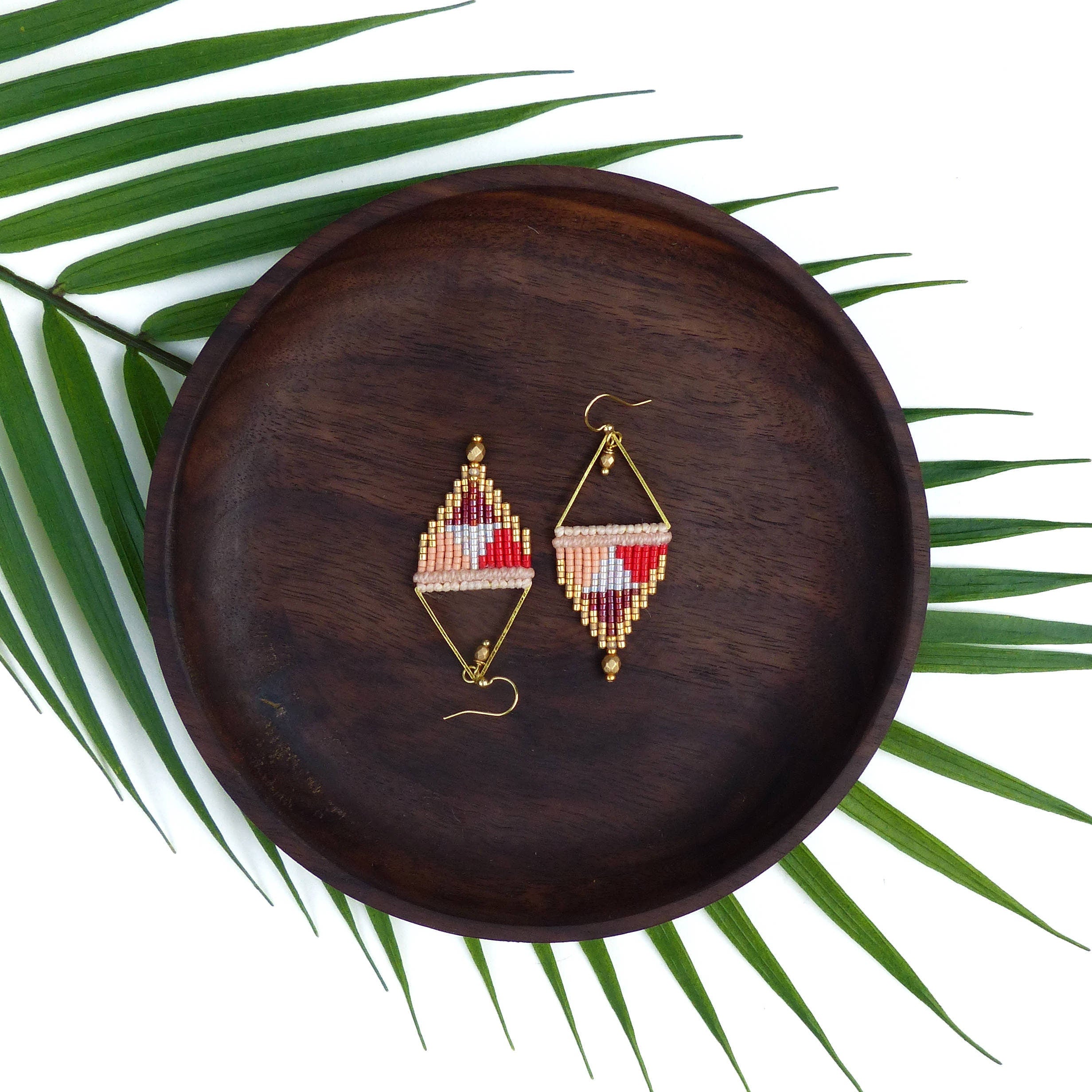 Peut inclure: Une paire de boucles d'oreilles en perles géométriques avec une finition dorée. Les boucles d'oreilles sont faites de perles rouges, roses et blanches et ont une forme triangulaire.