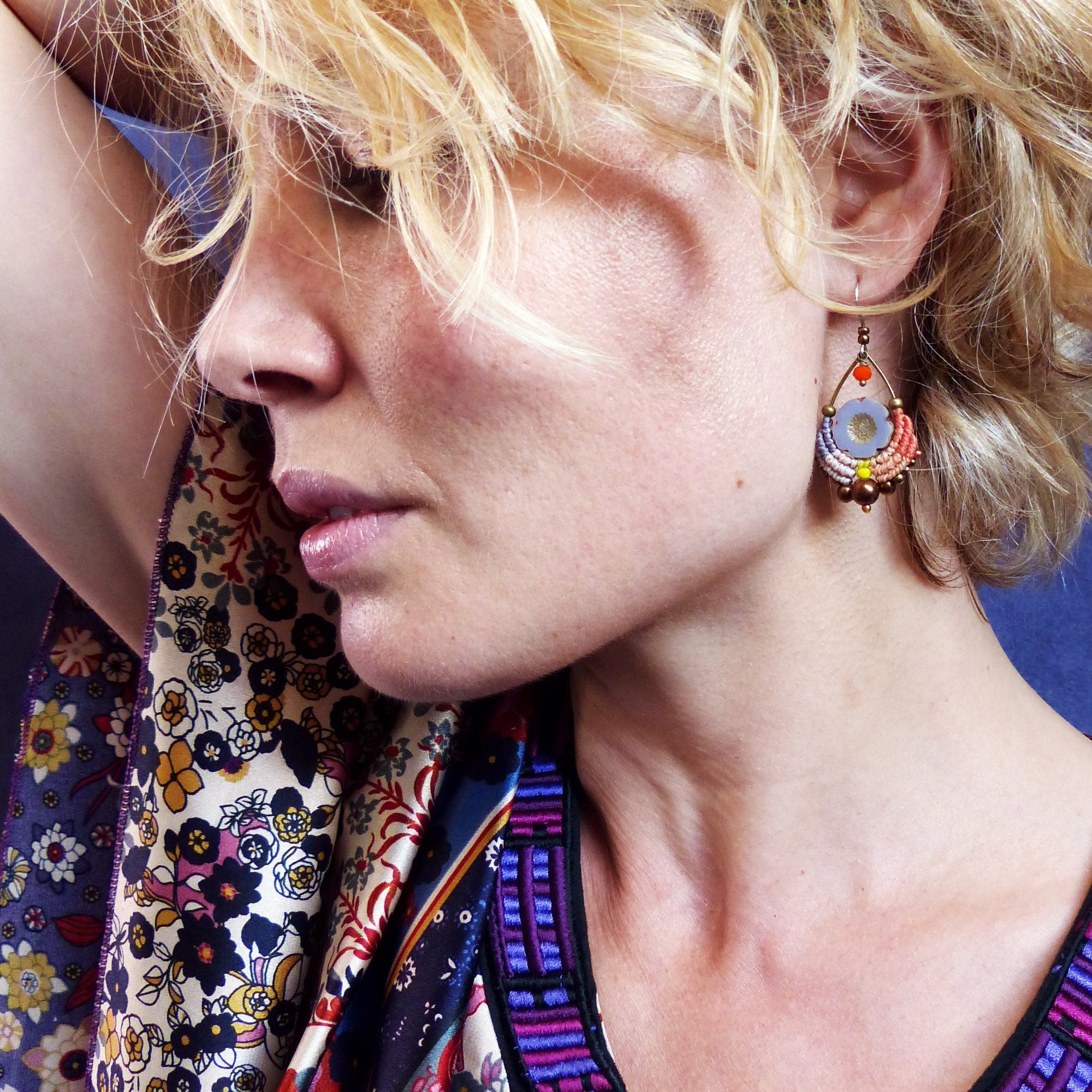 Peut inclure: Une femme aux cheveux blonds portant une écharpe à motifs colorés et des boucles d'oreilles avec un motif floral. Les boucles d'oreilles sont faites de perles et ont une finition bronze.