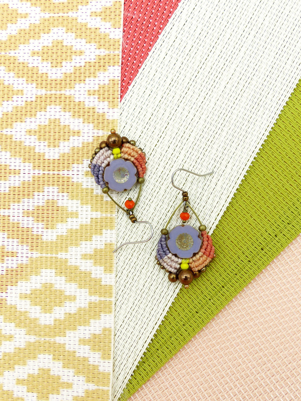 Peut inclure: Une paire de boucles d'oreilles en perles colorées avec un motif floral. Les boucles d'oreilles sont faites avec une variété de perles dans des tons de violet, orange, jaune et marron. Le motif floral est réalisé avec une perle violette au centre et entourée de perles plus petites dans des tons d'orange et de jaune.
