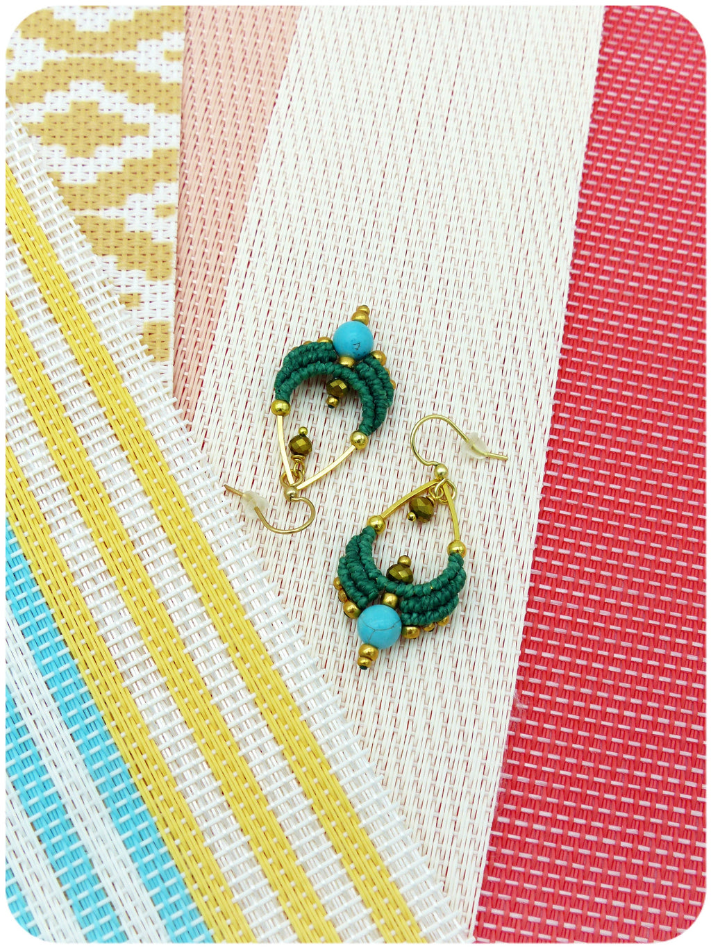 Peut inclure: Une paire de boucles d'oreilles vertes et dorées avec des perles turquoise. Les boucles d'oreilles sont suspendues sur un fond rayé blanc et rouge.