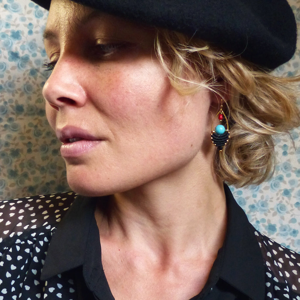 Peut inclure: Une femme portant un béret noir et une chemise à pois noirs et blancs avec une paire de boucles d'oreilles en or avec une perle turquoise et rouge.