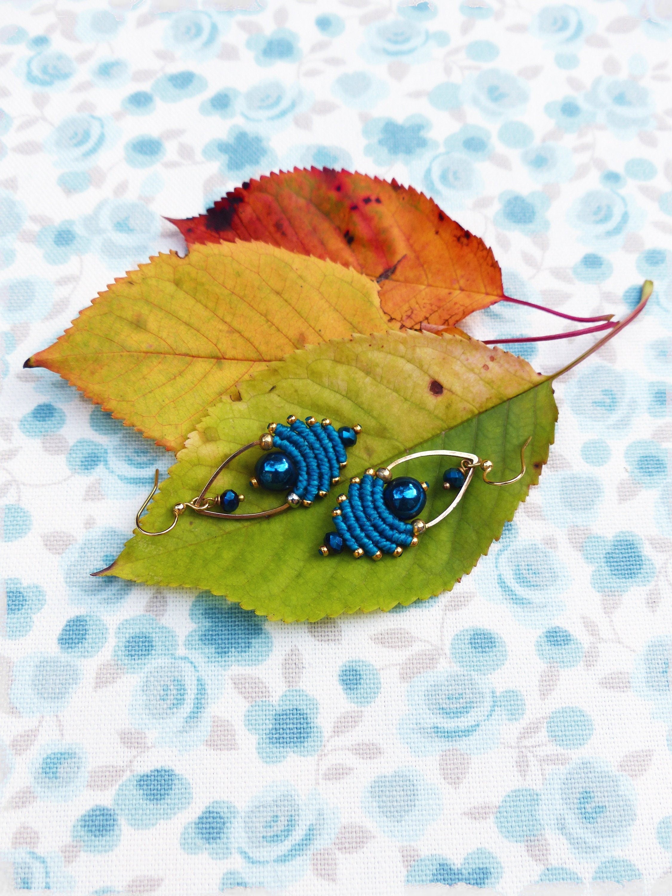 Peut inclure: Une paire de boucles d'oreilles bleues et dorées avec un motif perlé. Les boucles d'oreilles sont sur un fond blanc avec un motif floral.