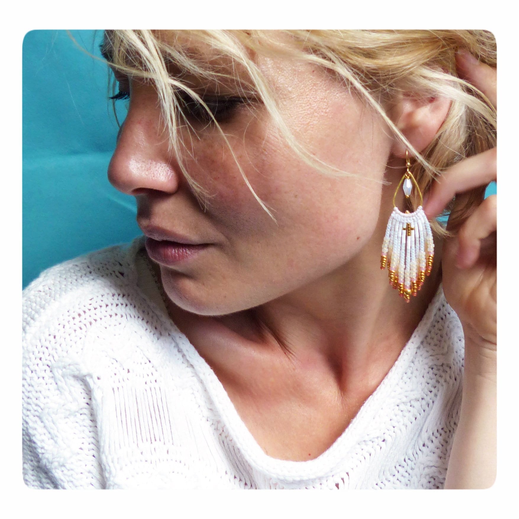 Peut inclure: Boucles d'oreilles en franges de perles blanches et dorées avec un petit charme en forme de croix. Les boucles d'oreilles sont pendantes et ont une forme de larme.