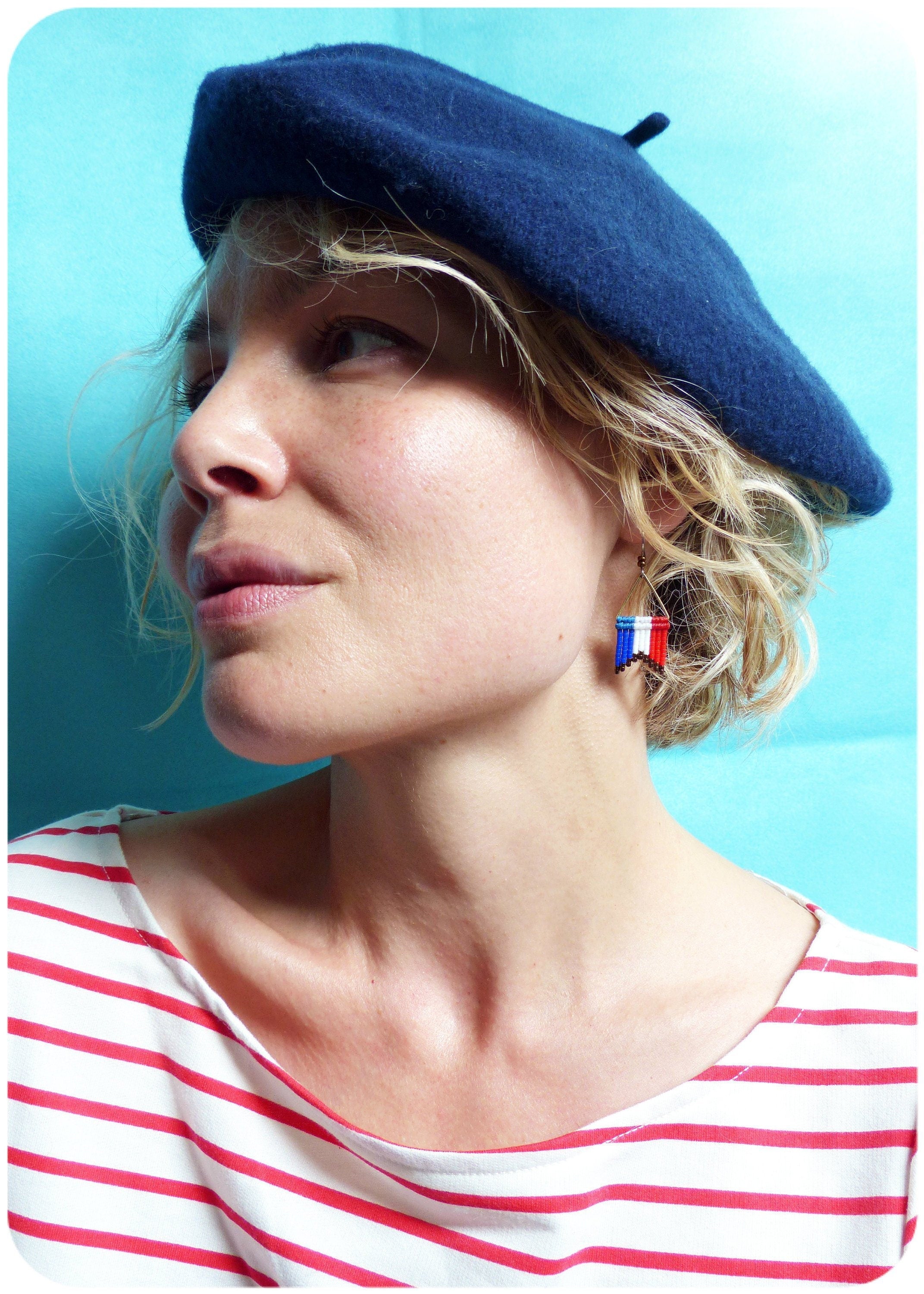 Peut inclure: Une femme portant un béret bleu marine et une chemise rayée rouge et blanche. Elle porte de petites boucles d'oreilles avec un motif de drapeau français.