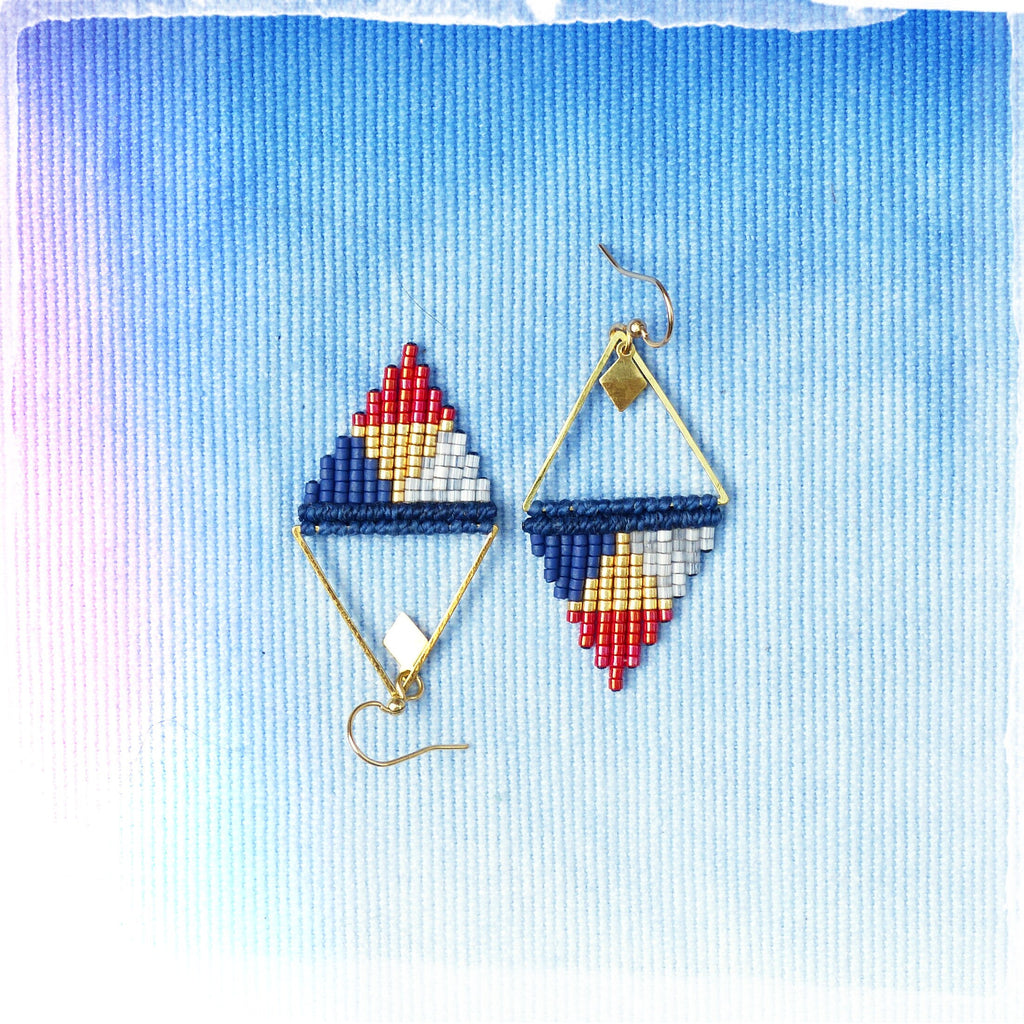 Peut inclure: Une paire de boucles d'oreilles triangulaires géométriques avec des accents rouge, blanc, bleu et or. Les boucles d'oreilles sont faites de petites perles et ont un cadre en fil d'or.