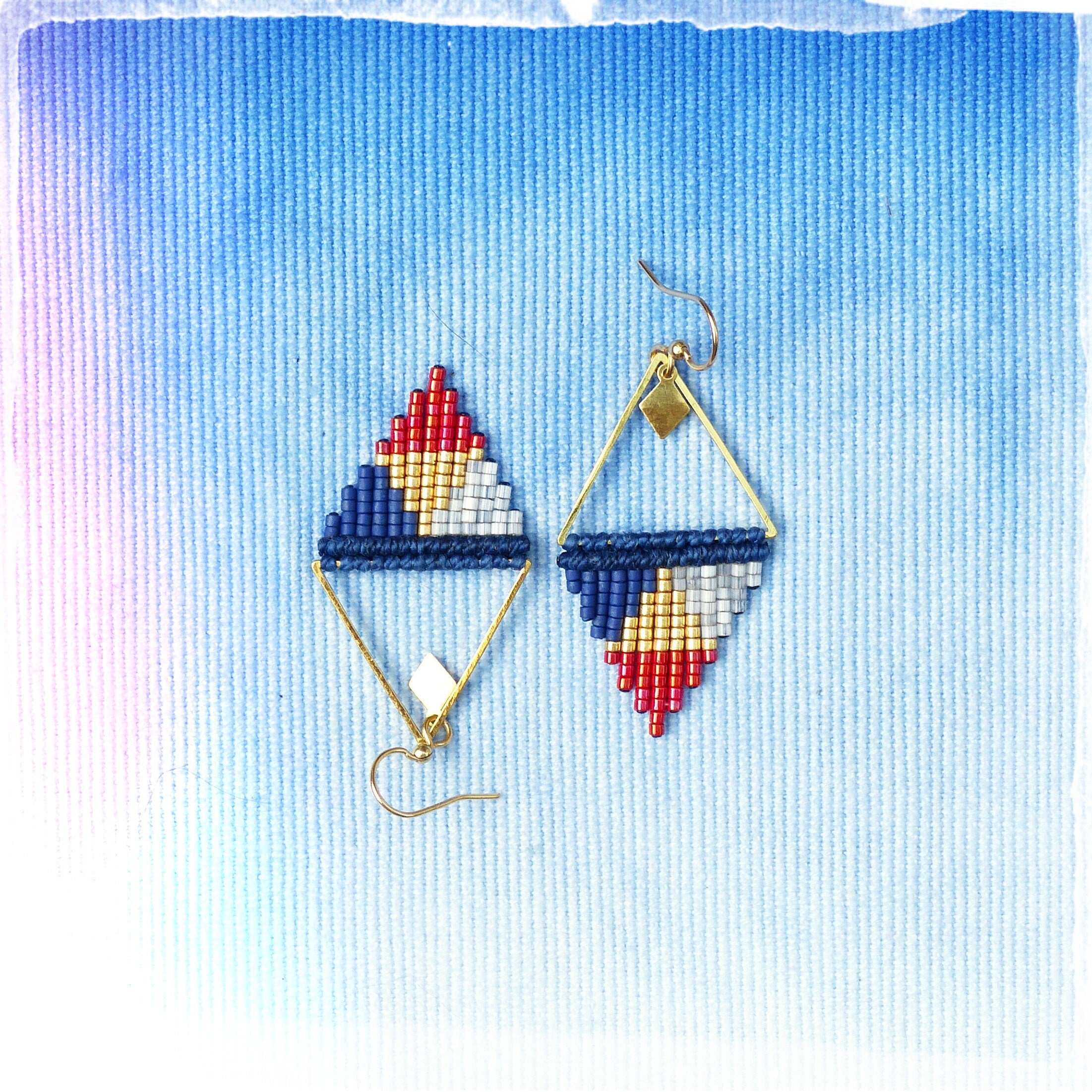 Peut inclure: Une paire de boucles d'oreilles triangulaires géométriques avec des accents rouge, blanc, bleu et or. Les boucles d'oreilles sont faites de petites perles et ont un cadre en fil d'or.