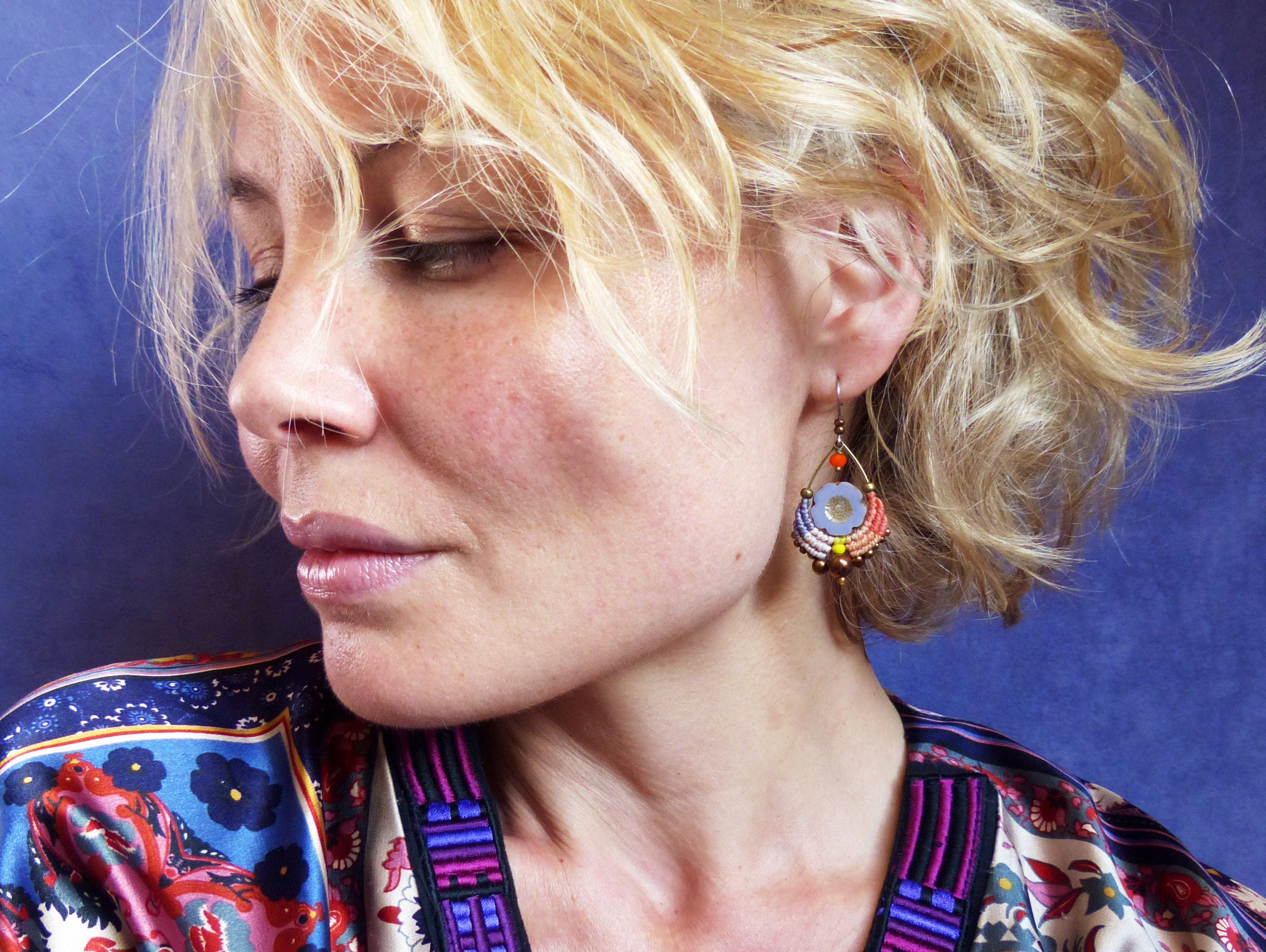 Peut inclure: Une femme aux cheveux blonds portant une chemise à motifs colorés et des boucles d'oreilles avec un motif de fleur violet, orange et jaune.