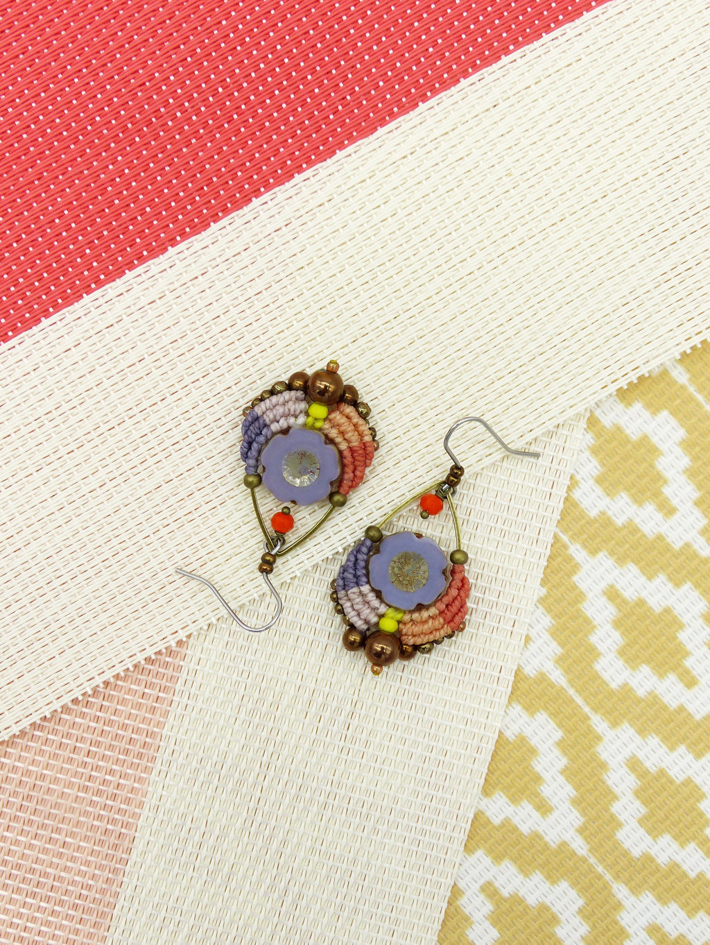 Peut inclure: Une paire de boucles d'oreilles en perles colorées avec un motif de fleur violette. Les boucles d'oreilles sont faites avec une variété de perles, y compris le brun, l'orange, le jaune et le rose. Les boucles d'oreilles sont suspendues à des crochets argentés.