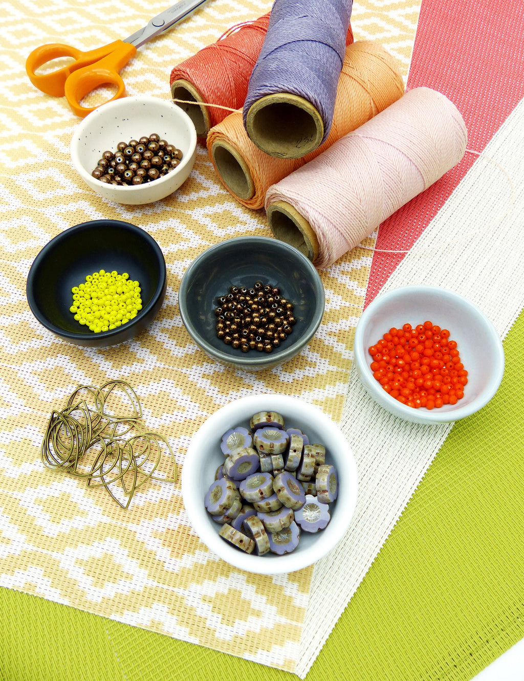 Peut inclure: Assortiment de perles colorées dans de petits bols, y compris des perles brunes, orange, jaunes et violettes. Il y a aussi des bobines de fil rose, orange et violet, et une paire de ciseaux.