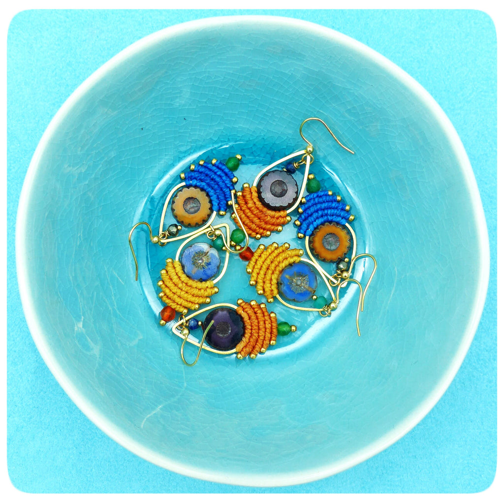 Peut inclure: Un ensemble de cinq boucles d'oreilles colorées avec des perles bleues, orange et jaunes et des accents dorés. Les boucles d'oreilles sont présentées dans un bol bleu.
