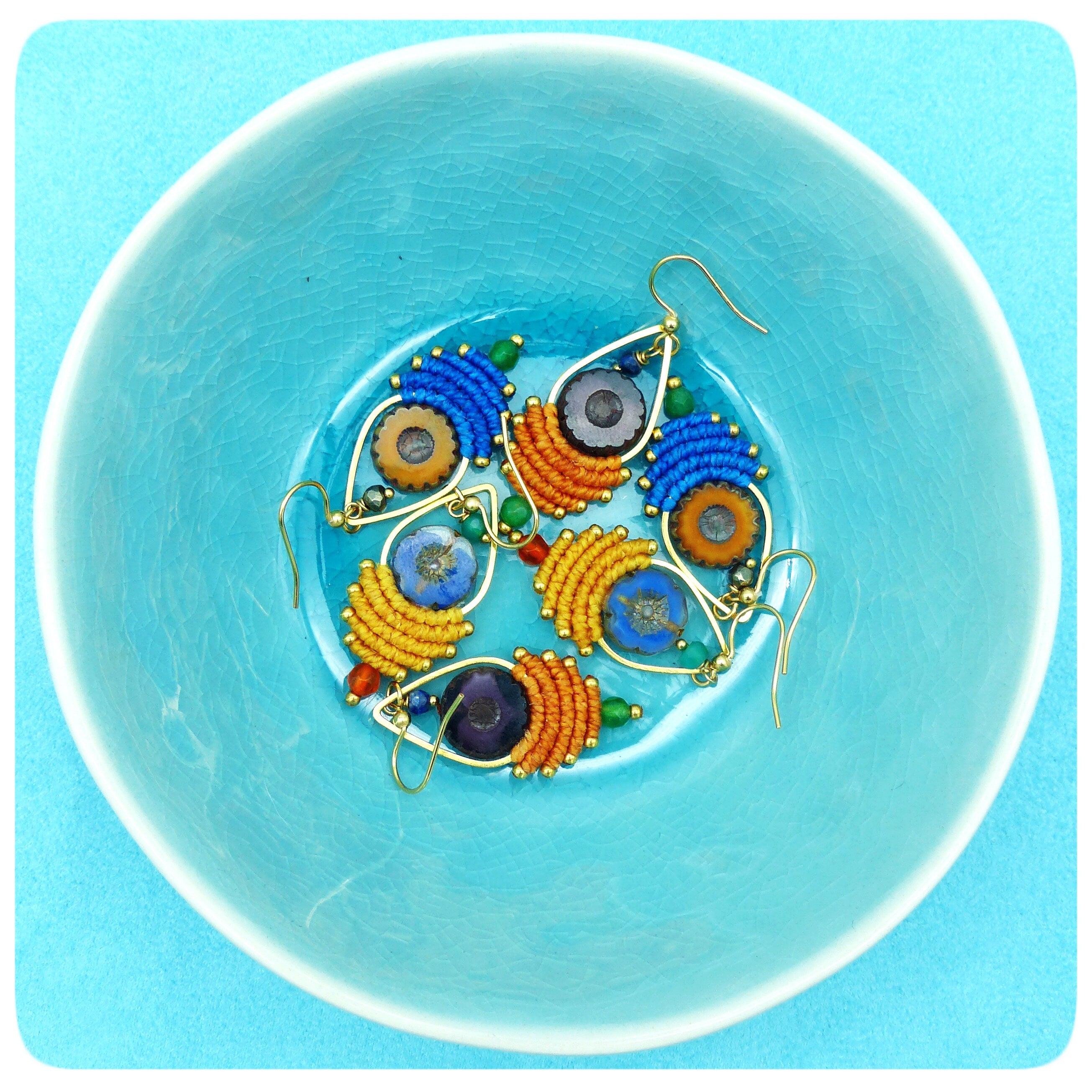 Peut inclure: Un ensemble de cinq boucles d'oreilles colorées avec des perles bleues, orange et jaunes et des accents dorés. Les boucles d'oreilles sont présentées dans un bol bleu.