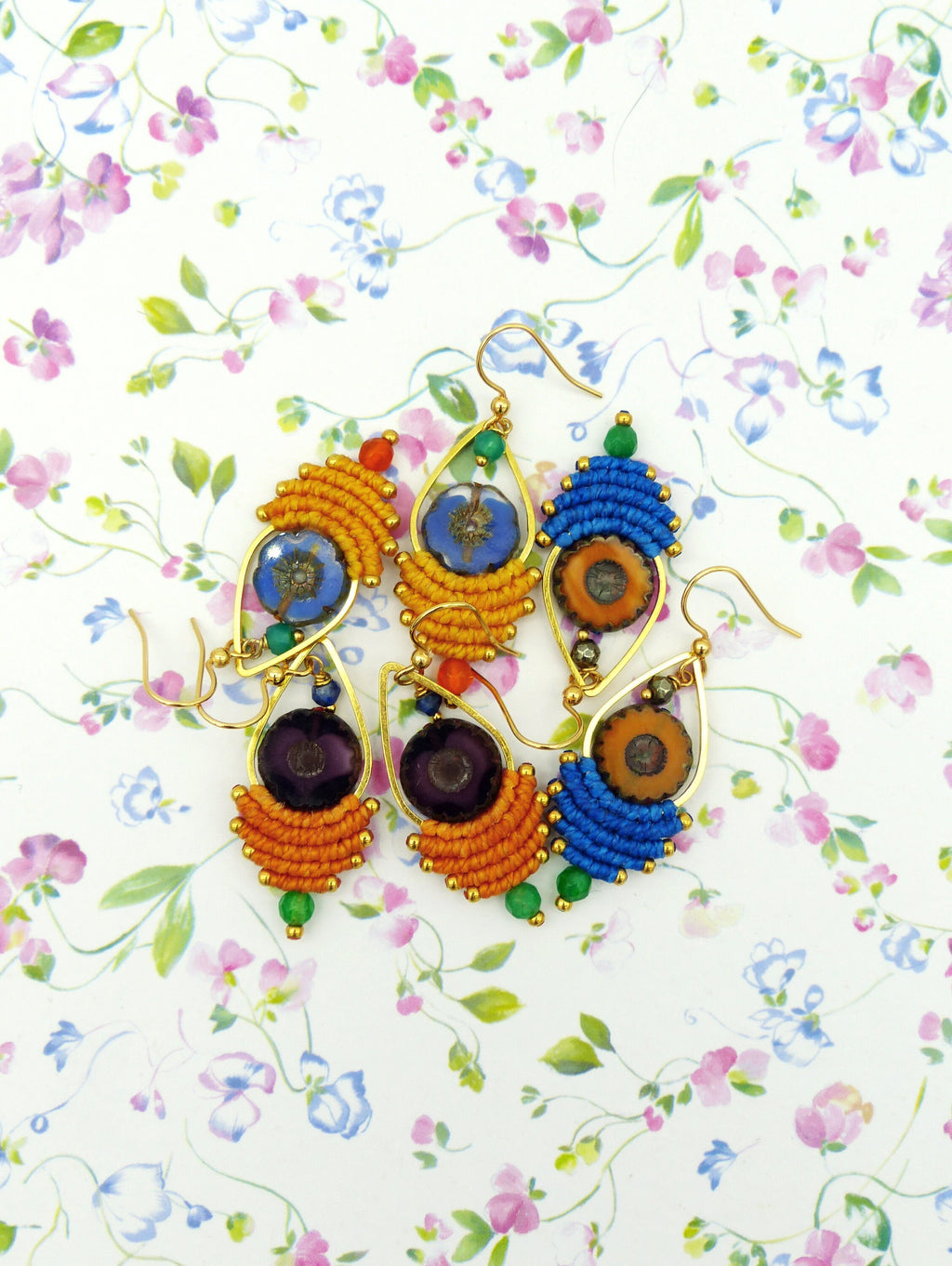 Peut inclure: Une paire de boucles d'oreilles faites à la main en forme de larme. Les boucles d'oreilles sont en macramé et présentent une variété de couleurs, notamment l'orange, le bleu, le vert et le violet. Chaque boucle d'oreille a une petite perle de verre ronde et transparente au centre.