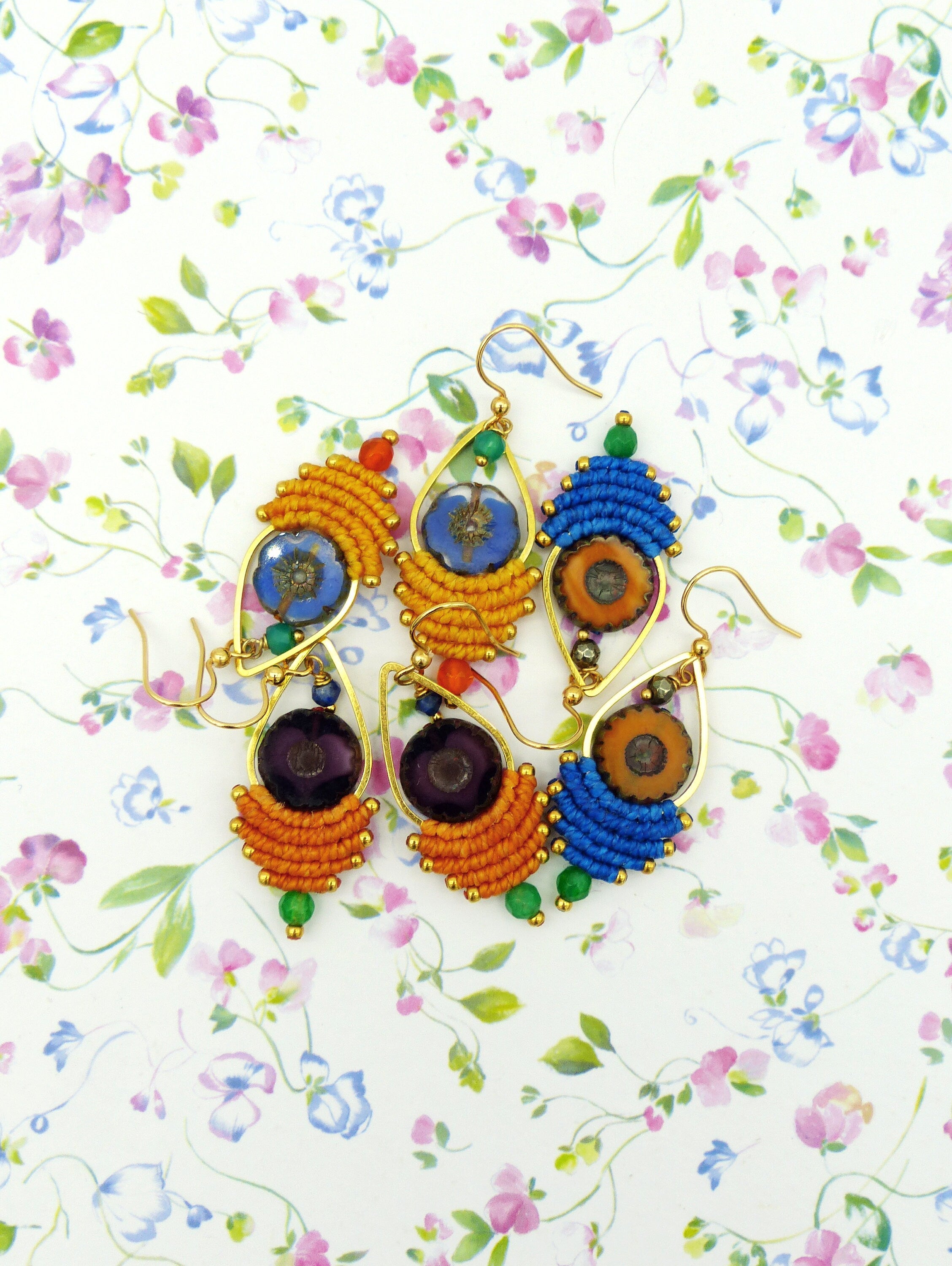 Peut inclure: Une paire de boucles d'oreilles faites à la main en forme de larme. Les boucles d'oreilles sont en macramé et présentent une variété de couleurs, notamment l'orange, le bleu, le vert et le violet. Chaque boucle d'oreille a une petite perle de verre ronde et transparente au centre.