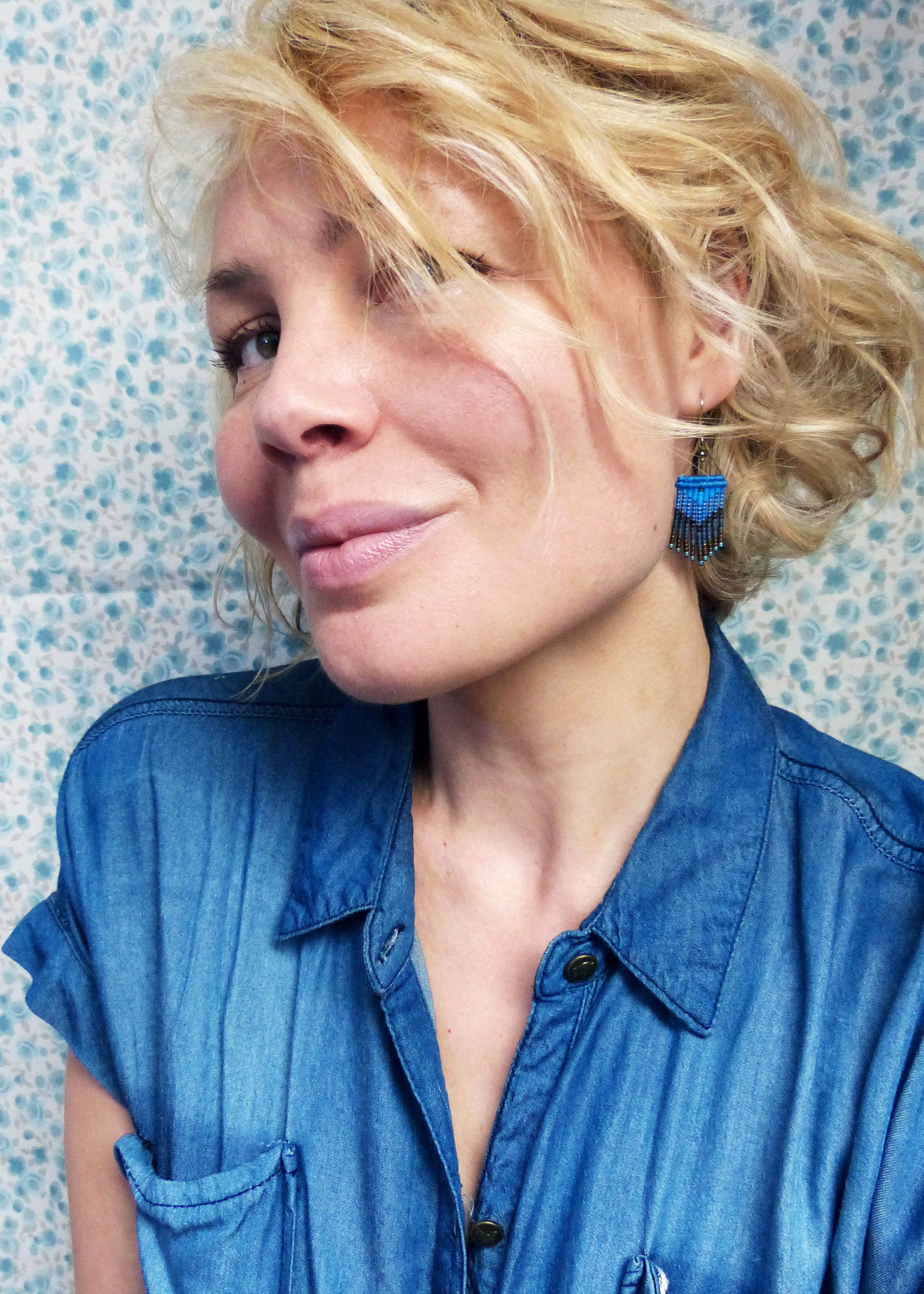 Peut inclure: Une femme aux cheveux blonds portant une chemise en jean bleu et des boucles d'oreilles en perles bleues. 