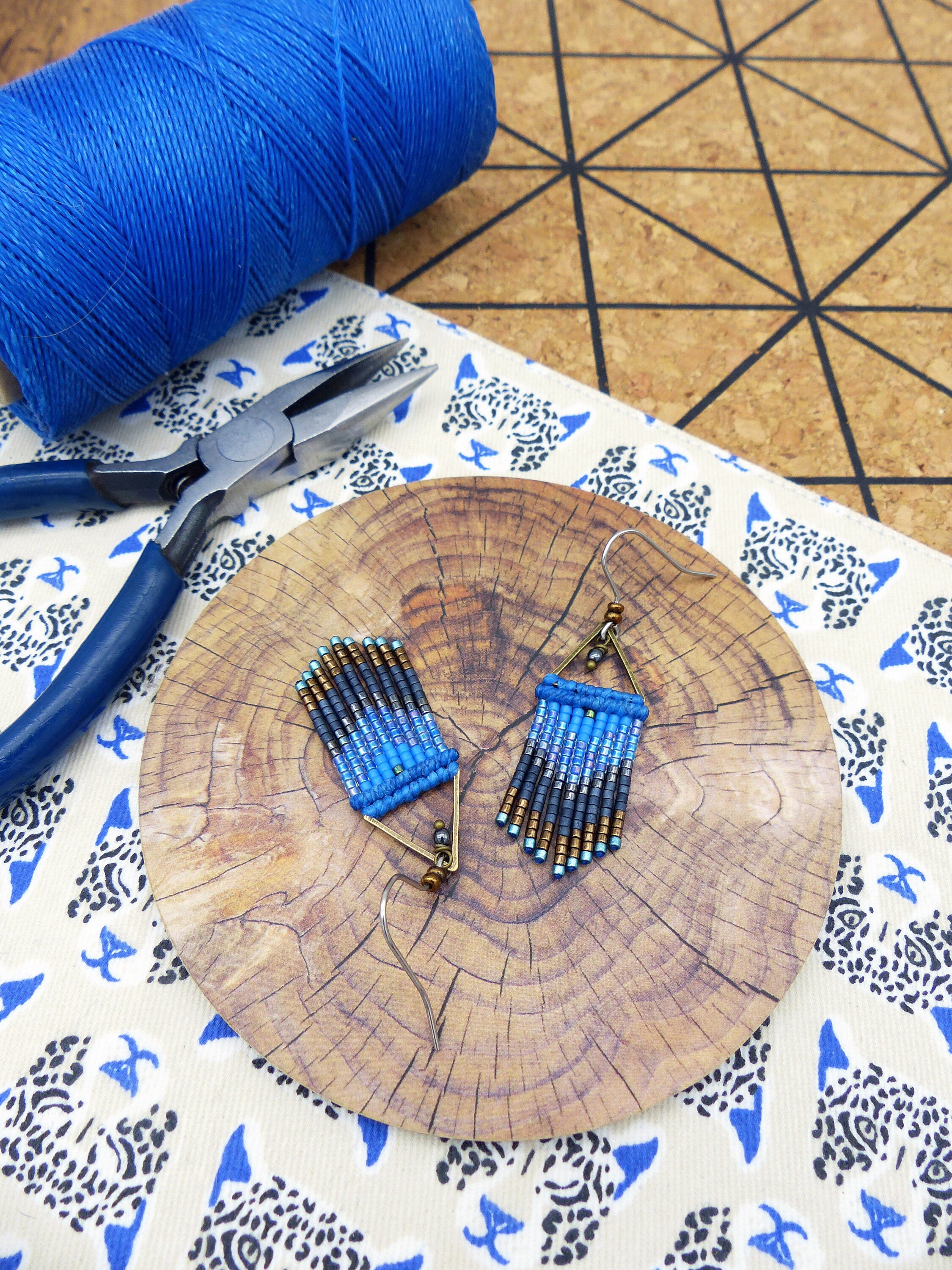 Peut inclure: Une paire de boucles d'oreilles en perles bleues et brunes de forme triangulaire avec un crochet en métal doré. Les boucles d'oreilles sont présentées sur une surface en bois.