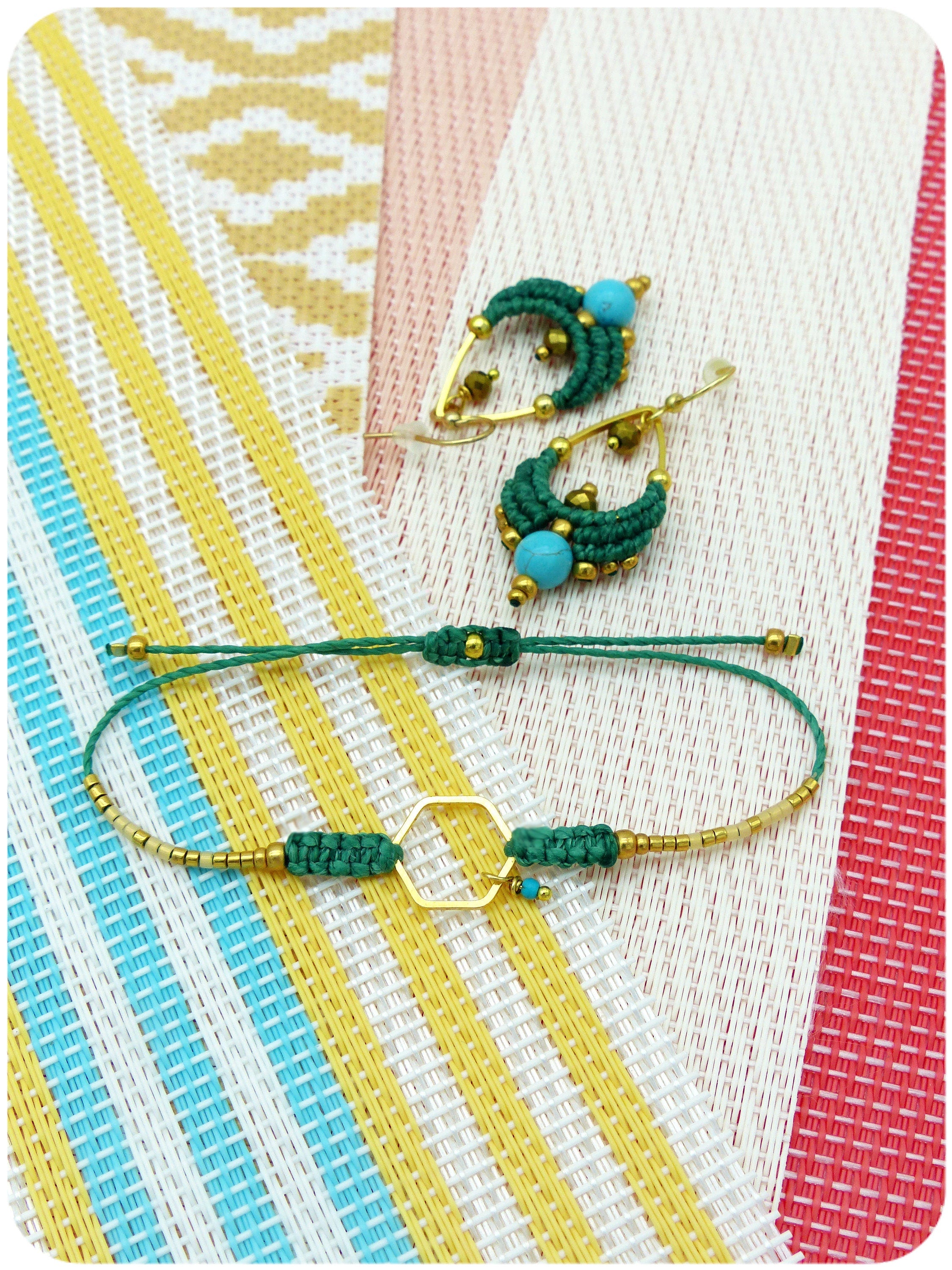 Peut inclure: Un ensemble de boucles d'oreilles en perles vertes et turquoise et un bracelet assorti avec un charme hexagonal doré. Les bijoux sont présentés sur un fond rayé coloré.