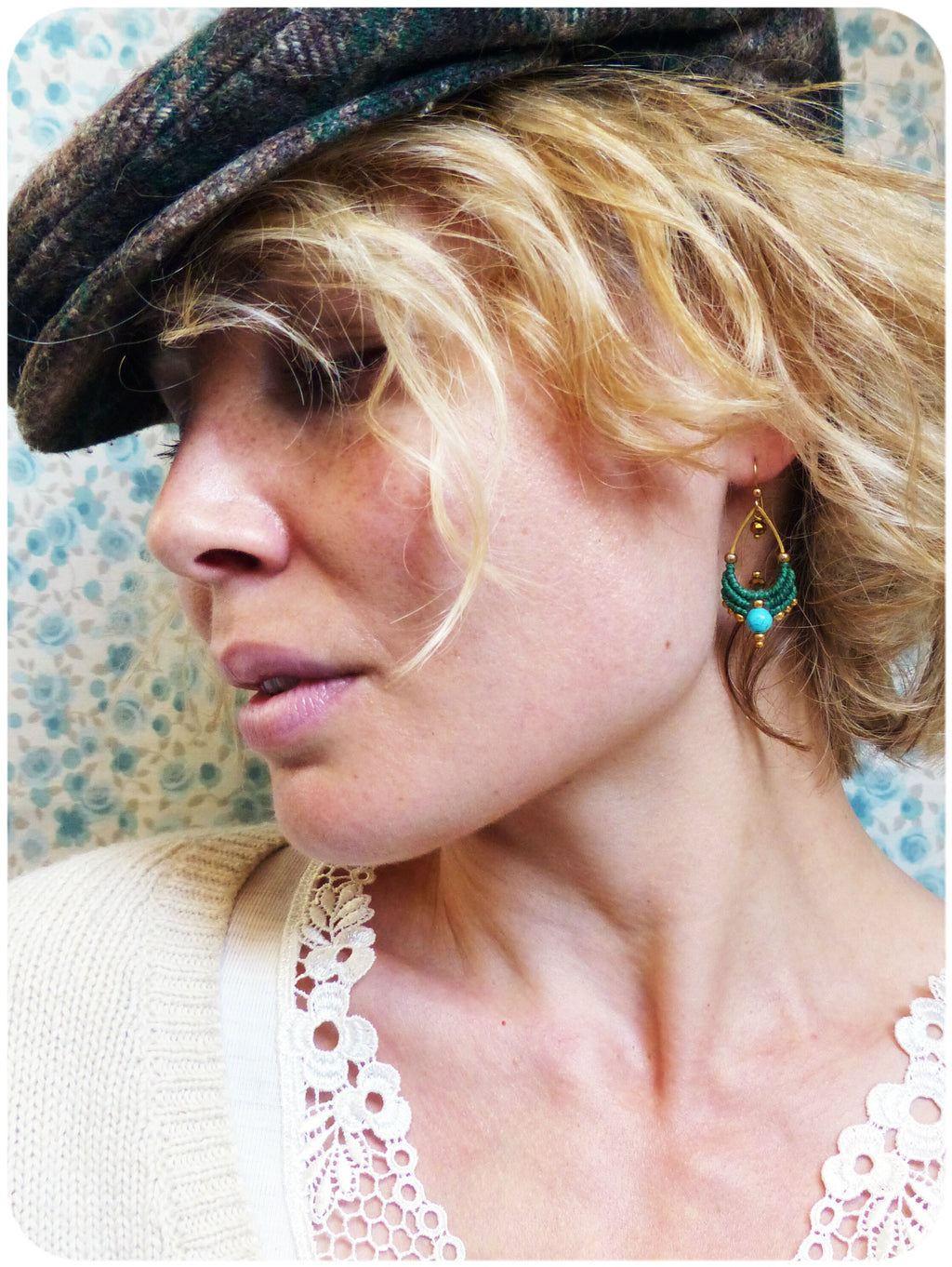 Peut inclure: Une femme aux cheveux blonds portant une casquette de nouvelles en tissu marron et un haut en crochet blanc avec une boucle d'oreille pendante en turquoise et or.