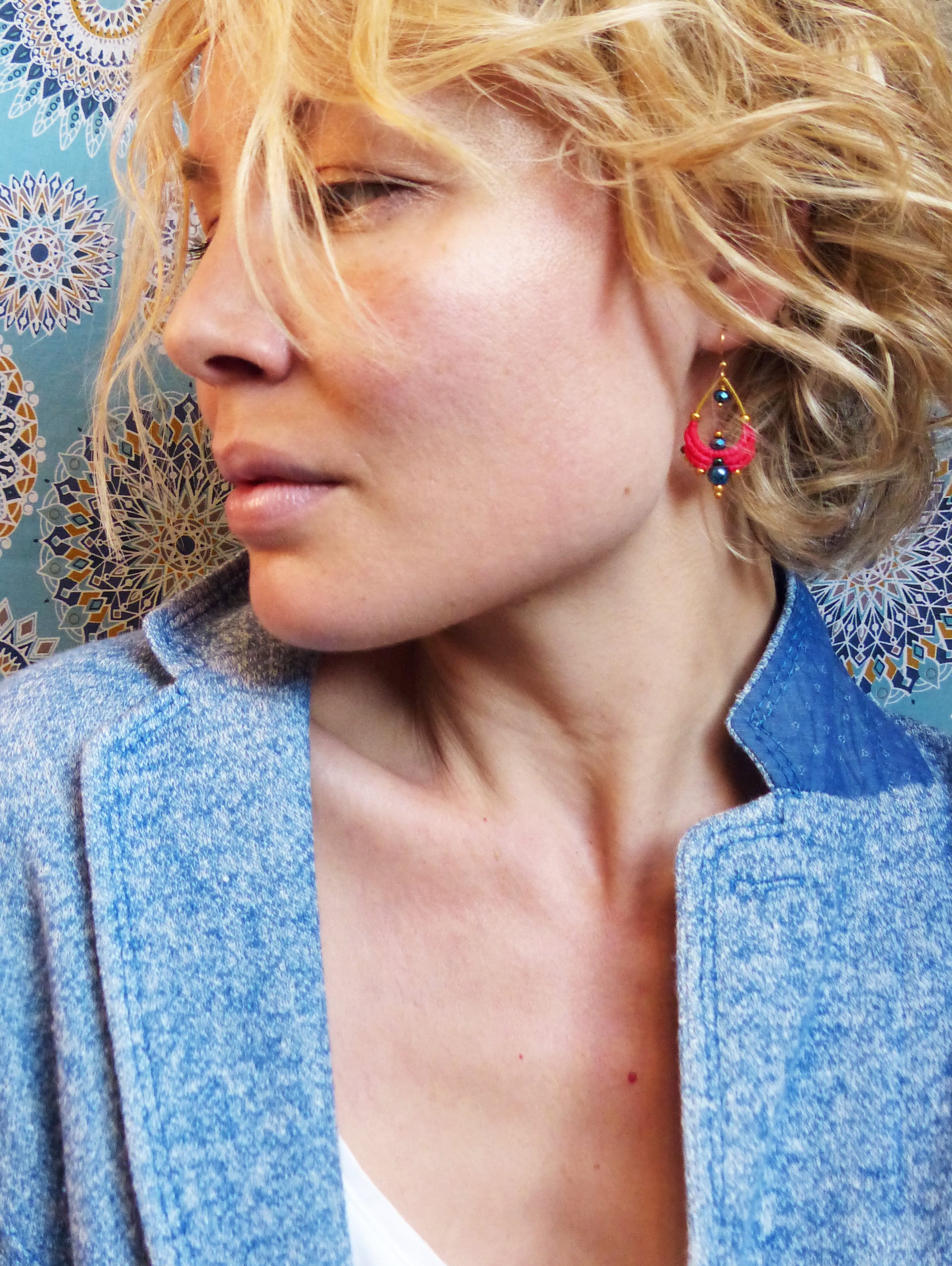 Peut inclure: Une femme aux cheveux blonds portant une veste bleue et des boucles d'oreilles avec des perles roses et bleues. Les boucles d'oreilles sont en or et ont une forme de larme.