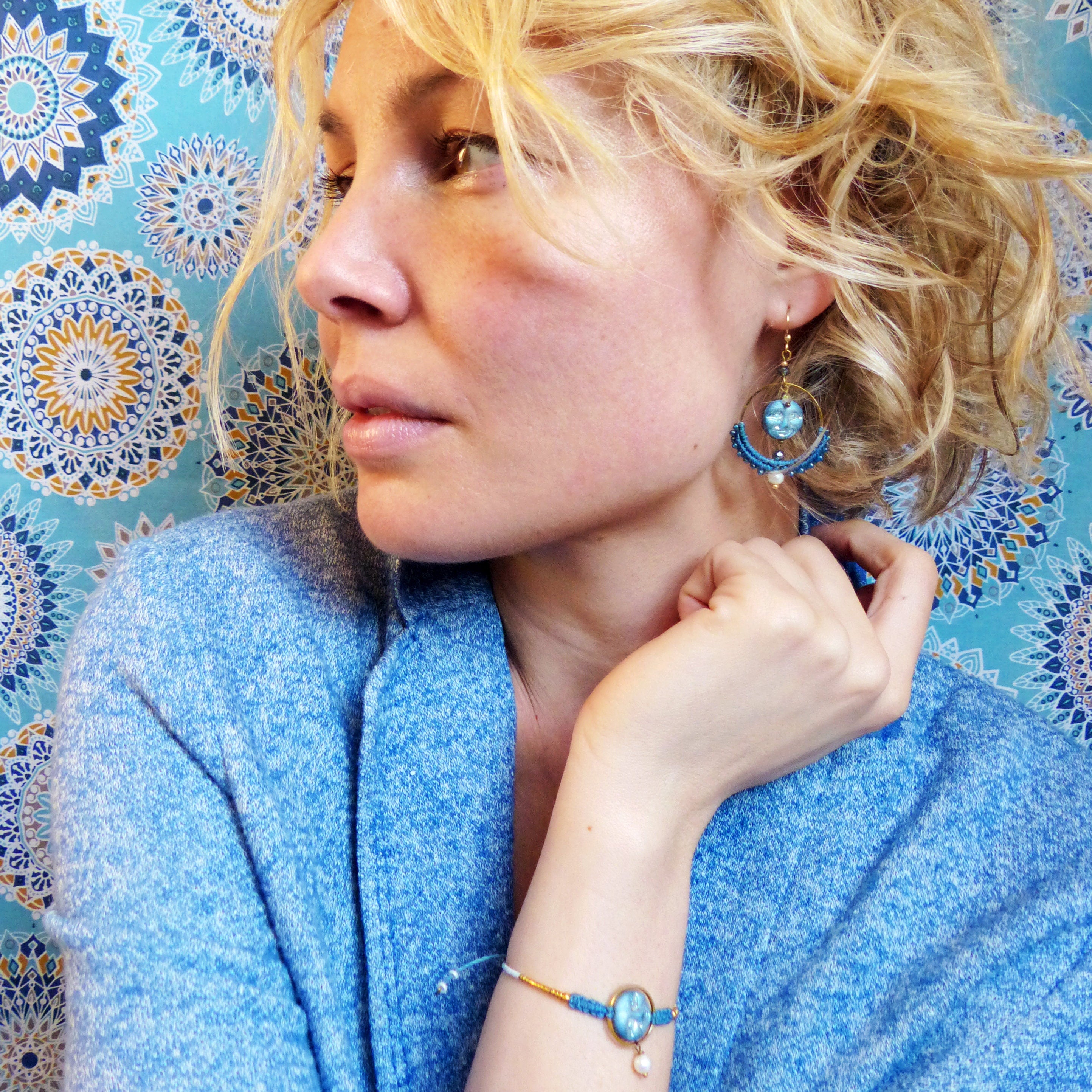 Peut inclure: Une femme portant un pull bleu avec un bracelet bleu et or avec un charme de perle. Elle porte également des boucles d'oreilles bleues et or avec un charme de perle.