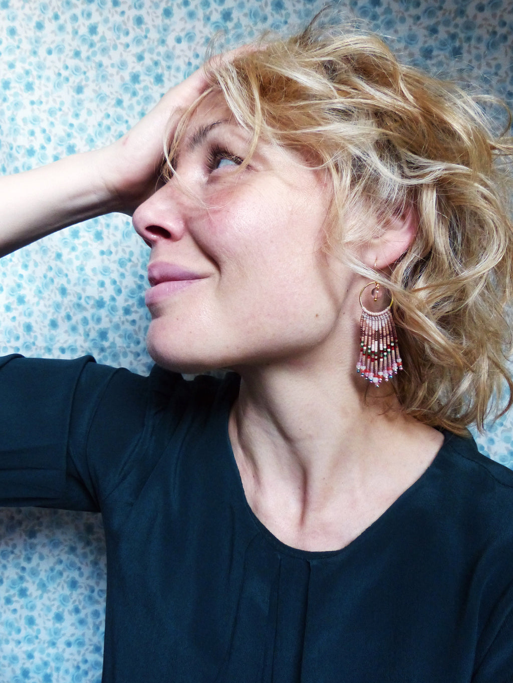 Peut inclure: Une femme aux cheveux blonds portant une chemise vert foncé et de longues boucles d'oreilles en perles avec des accents roses, rouges et dorés.