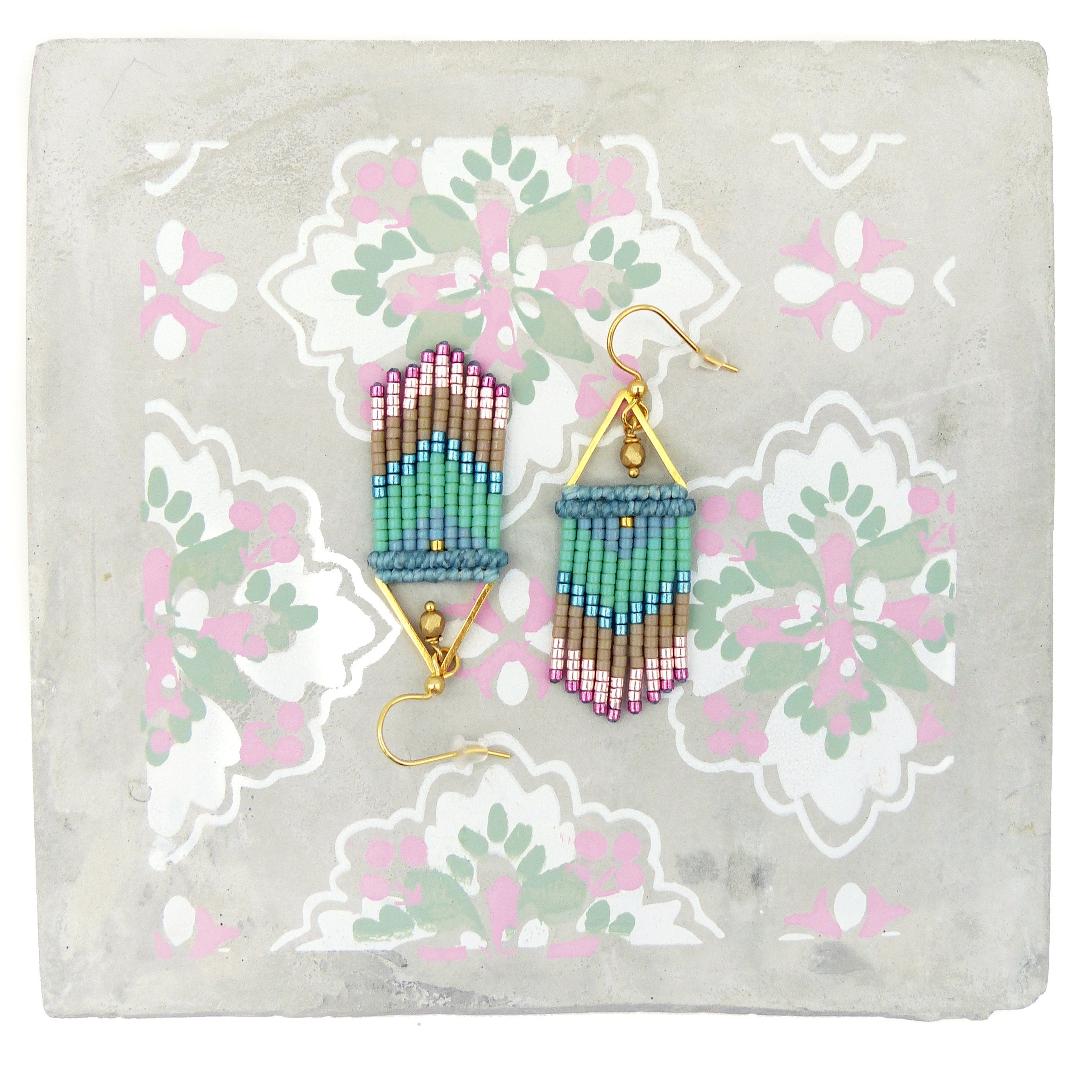 Peut inclure: Une paire de boucles d'oreilles pendantes dorées avec un motif géométrique. Les boucles d'oreilles sont faites de petites perles dans des tons de rose, bleu, vert et marron.