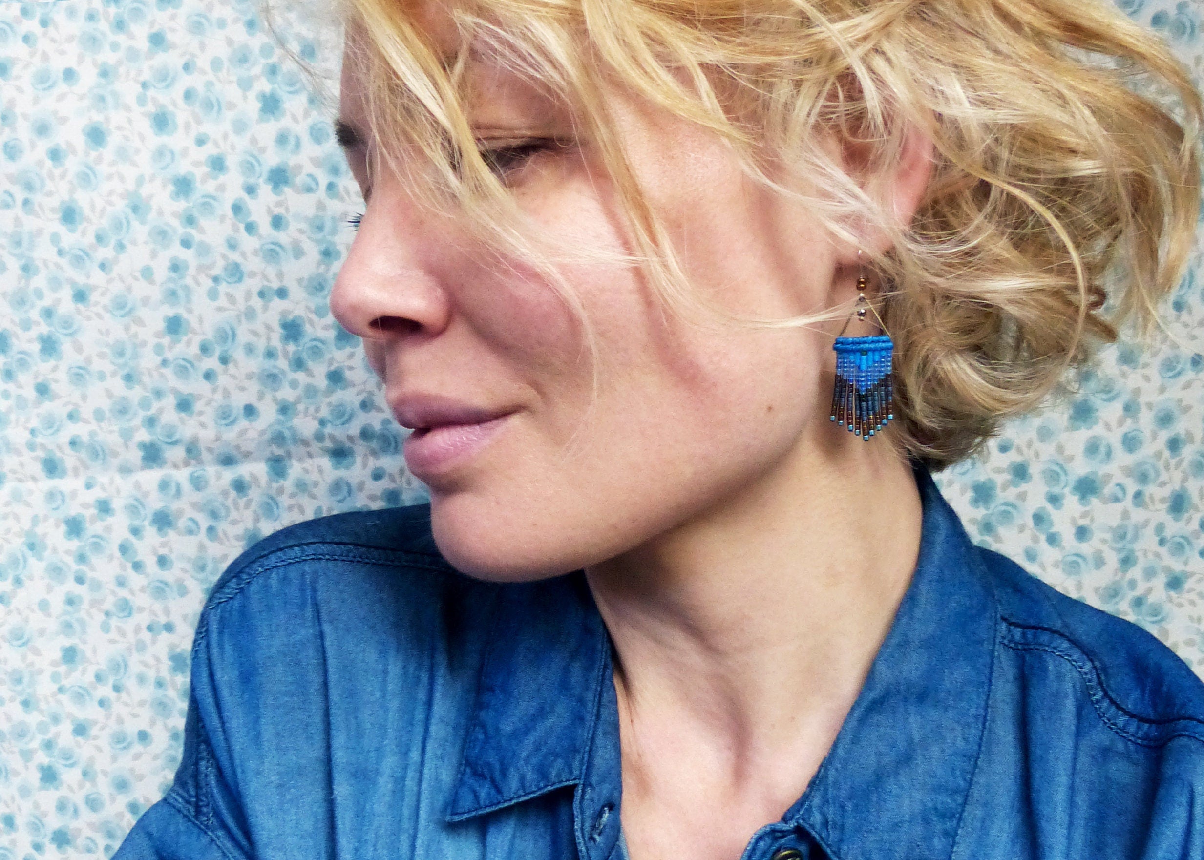 Peut inclure: Une femme aux cheveux blonds portant une chemise en jean bleue et des boucles d'oreilles en perles bleues et brunes.